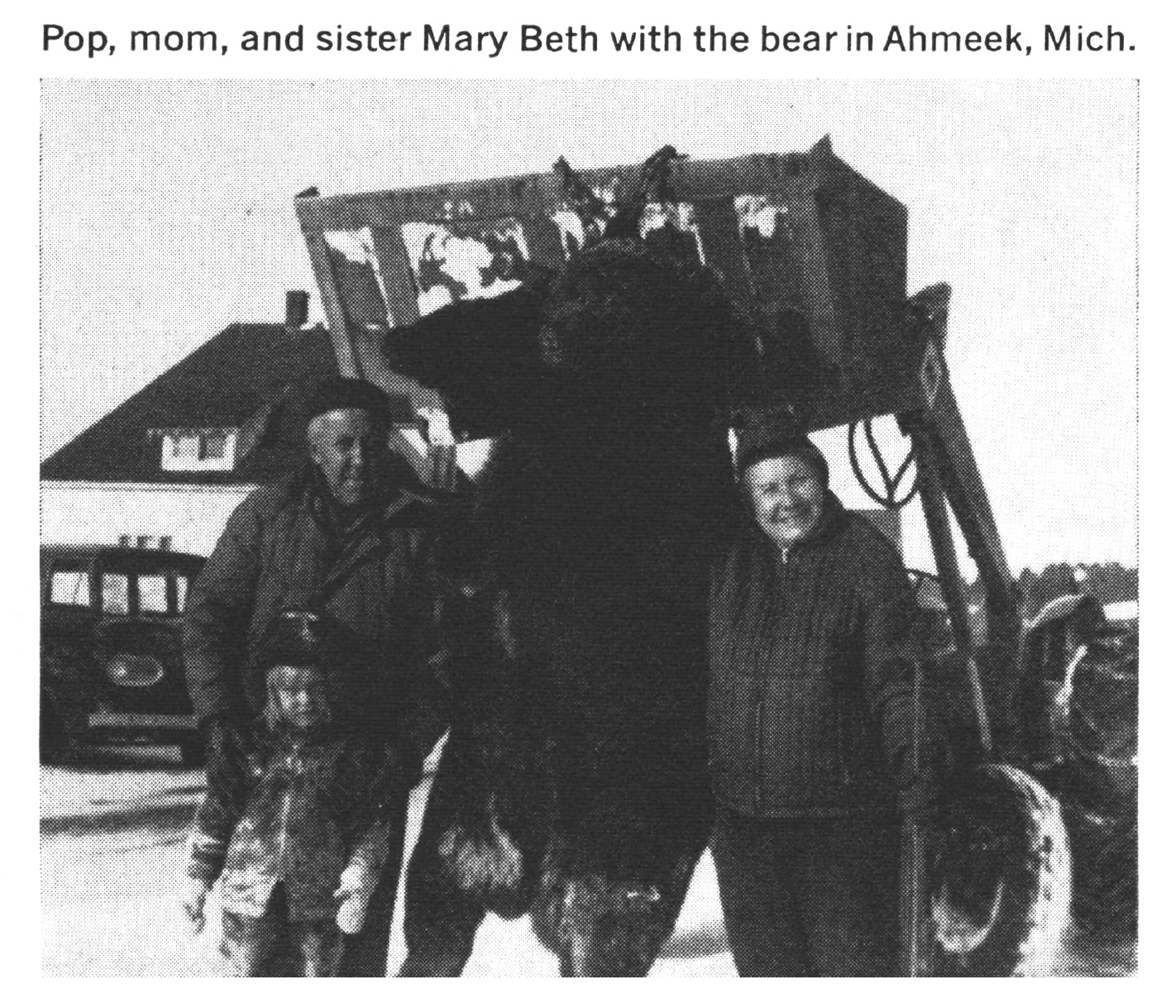 A family poses by a black bear on a tractor bucket in a black and white photo.