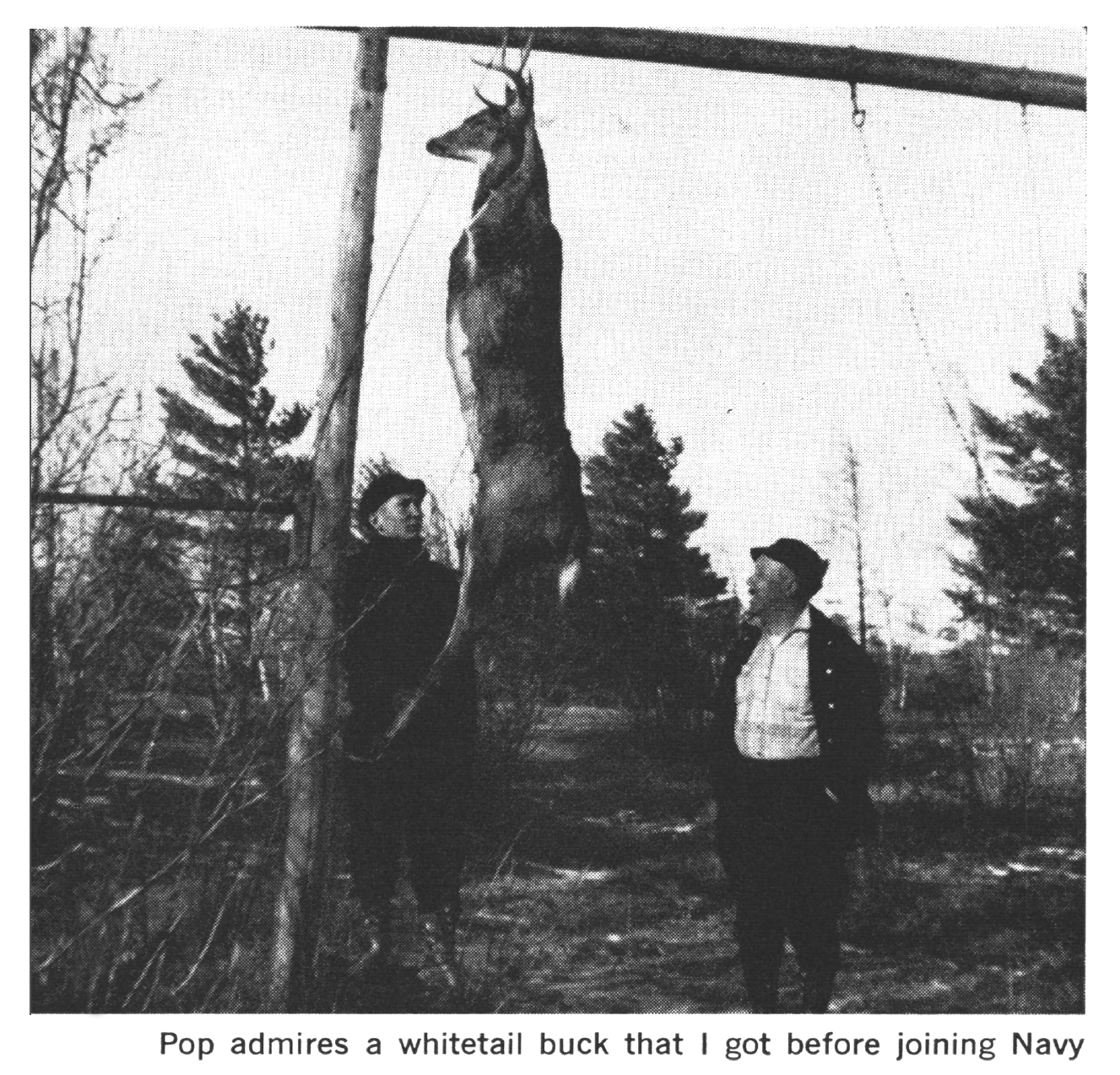 A black and white photograph of two men admiring a buck on a meat pole.