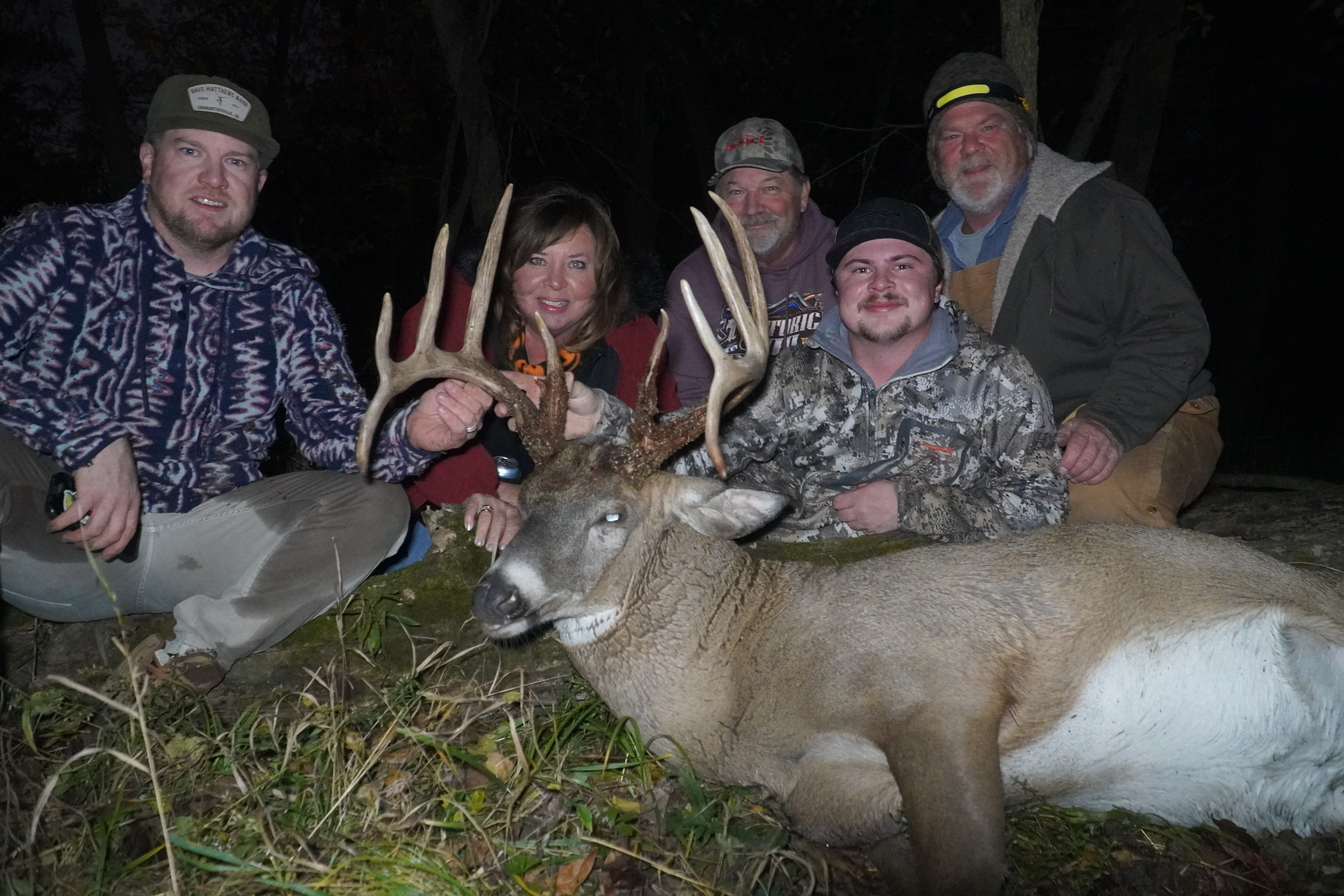 A group of people pose with a large 13-point buck with double drop tines.