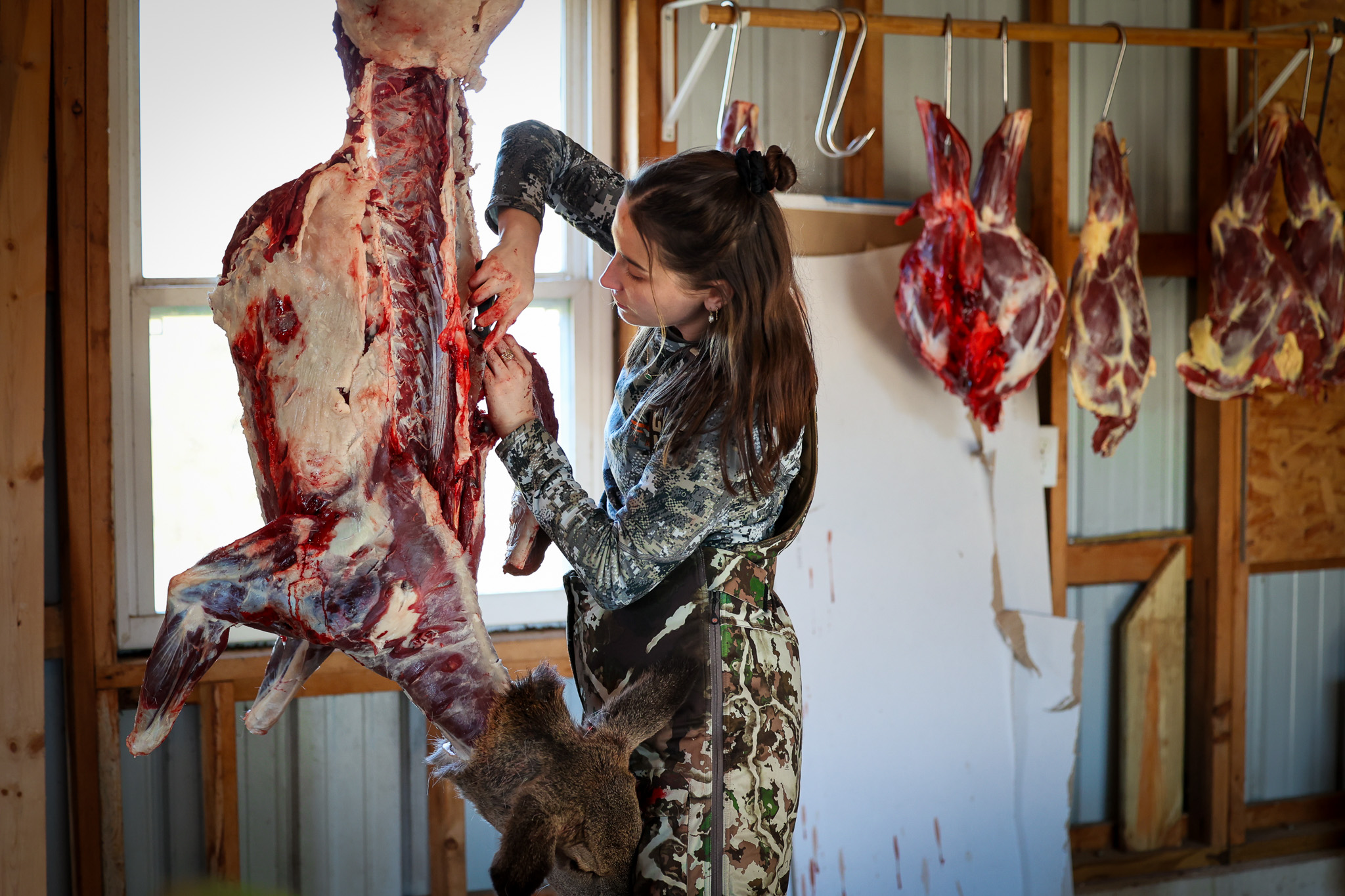 A hunter butchers a deer hanging in a skinning shed.