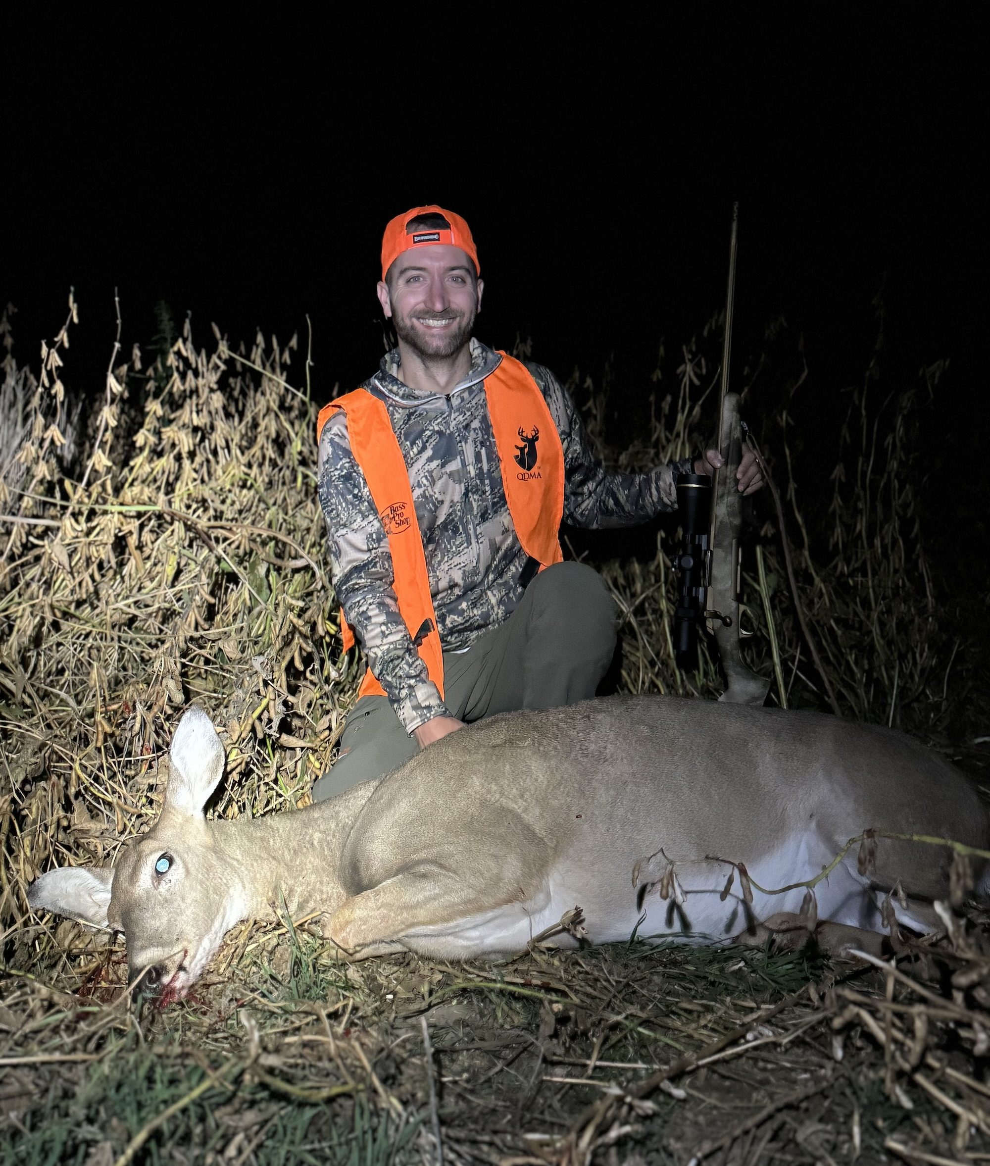 A hunter kneels beside a doe in a bean field.