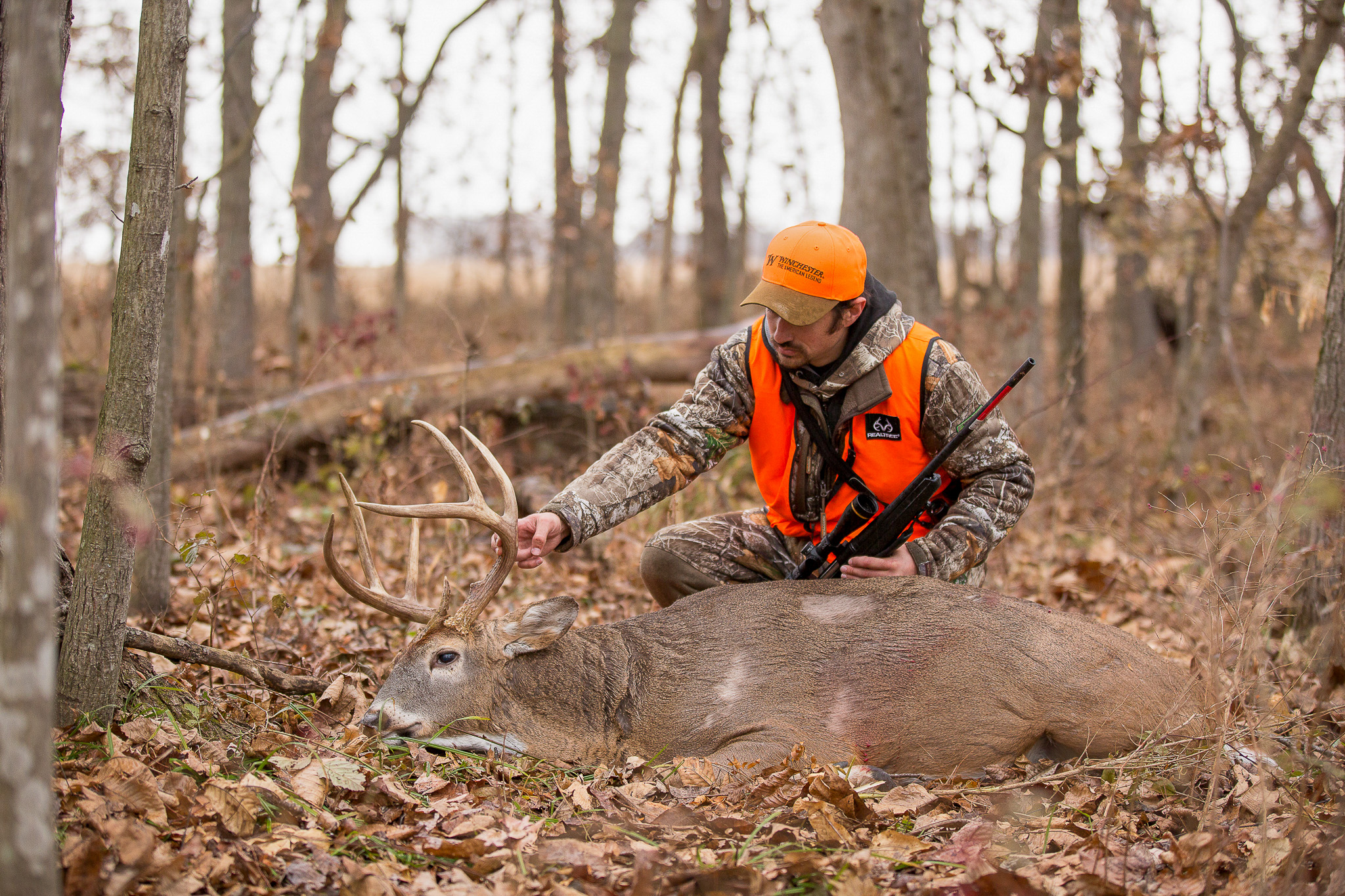 A hunter examines the antlers of a buck in the timber.