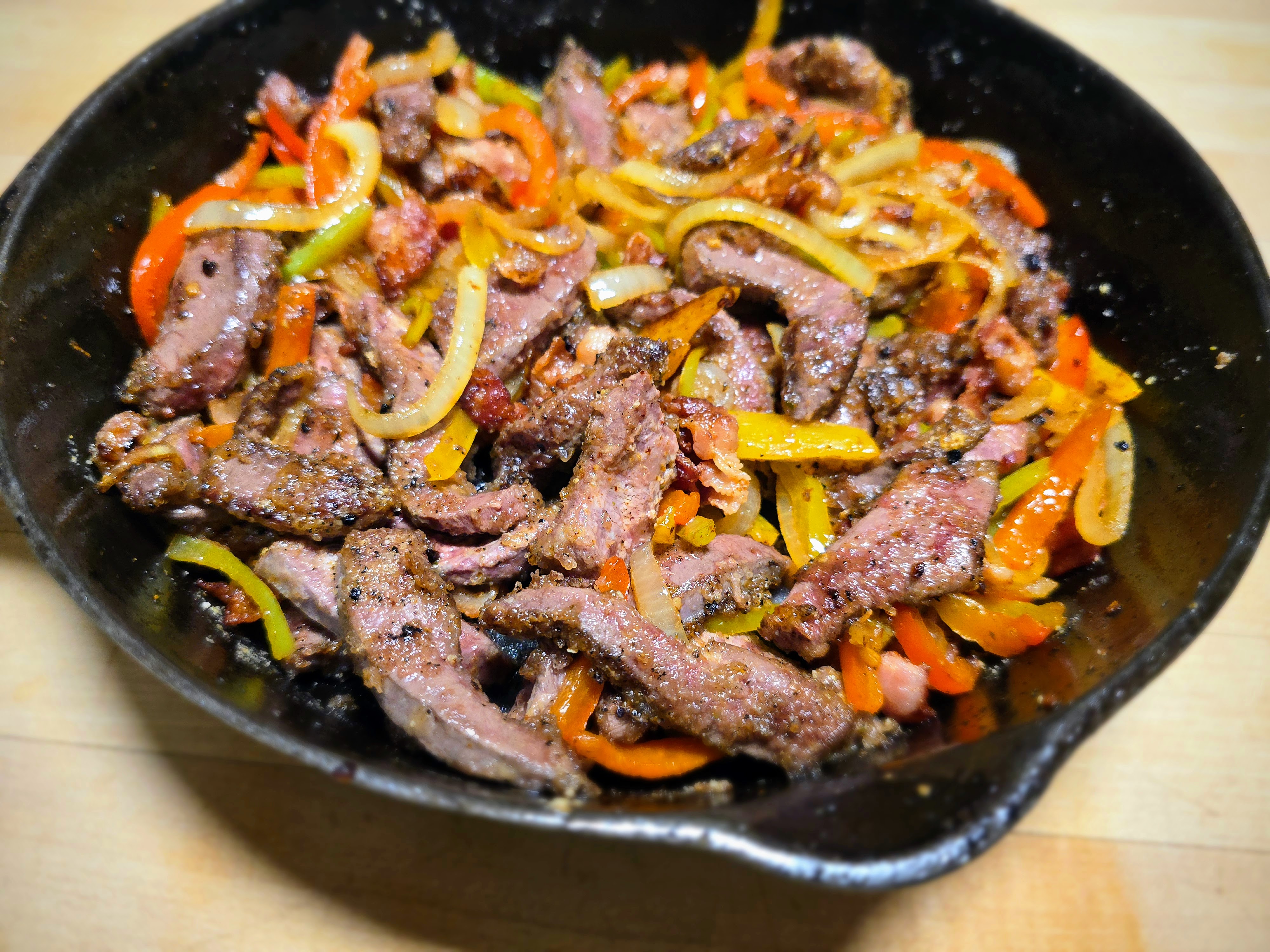 A cast iron skill filled with sliced meat and veggies.