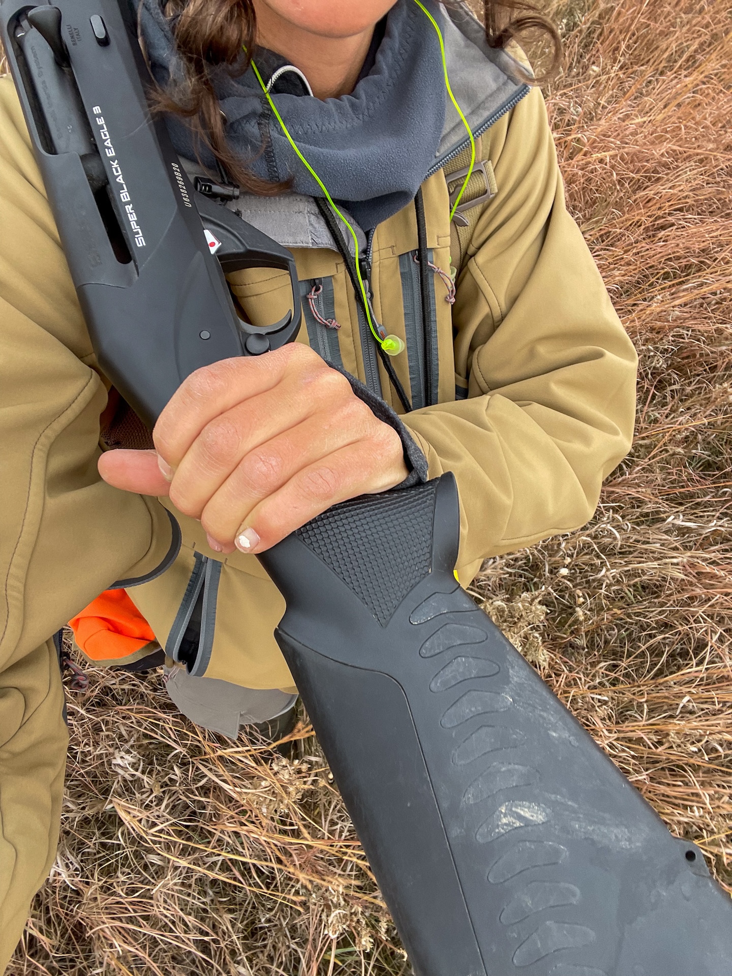 A downward view of a woman holding a shotgun and wearing a tan jacket