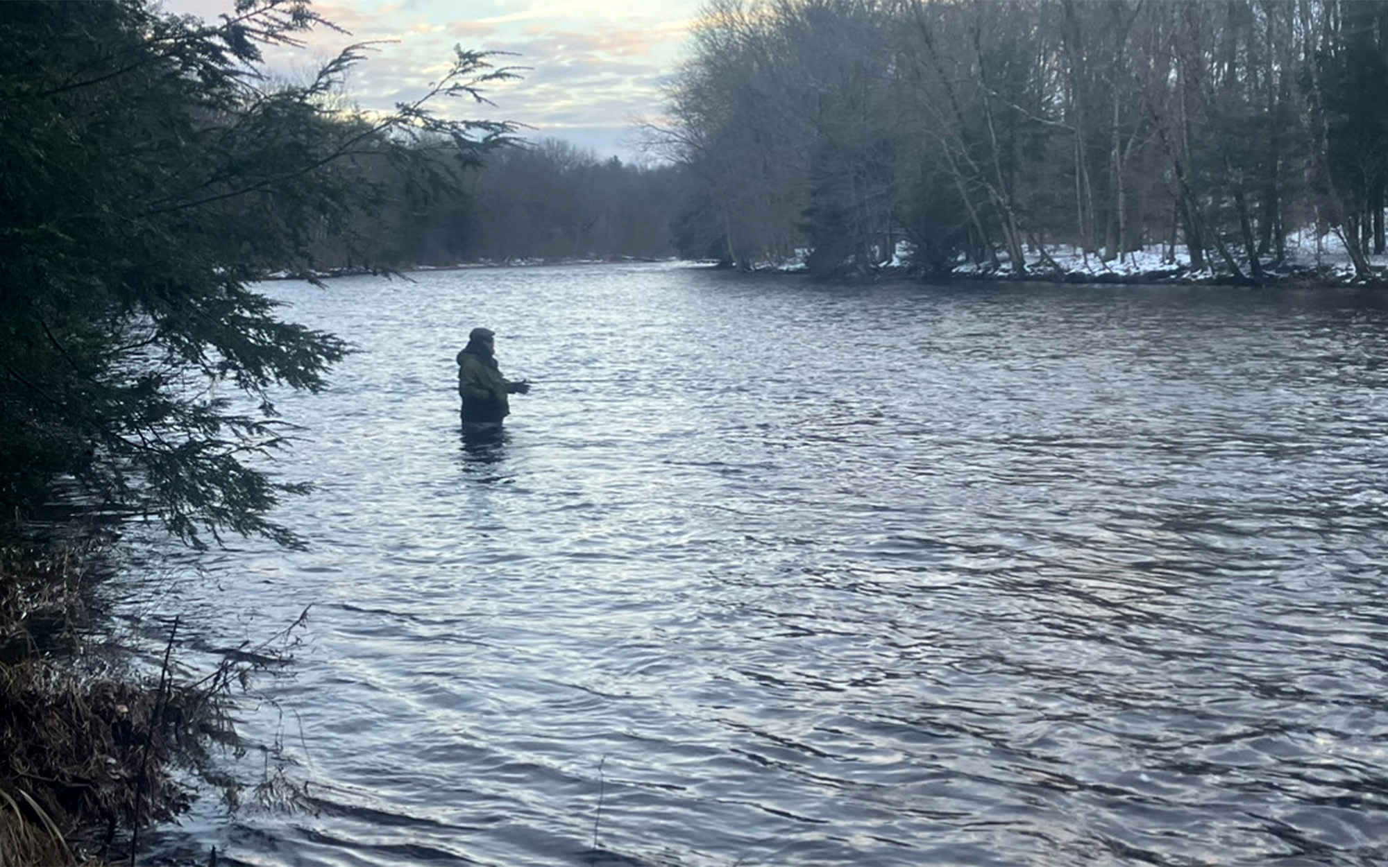 An angler swings a fly in a broad river.