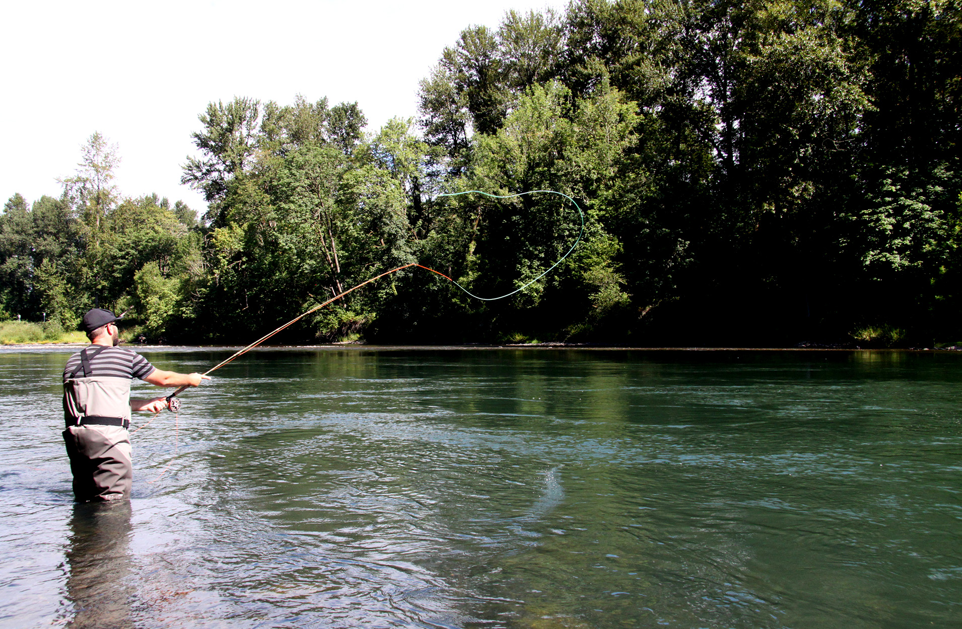 An angler casts a two-handed rod in a river.