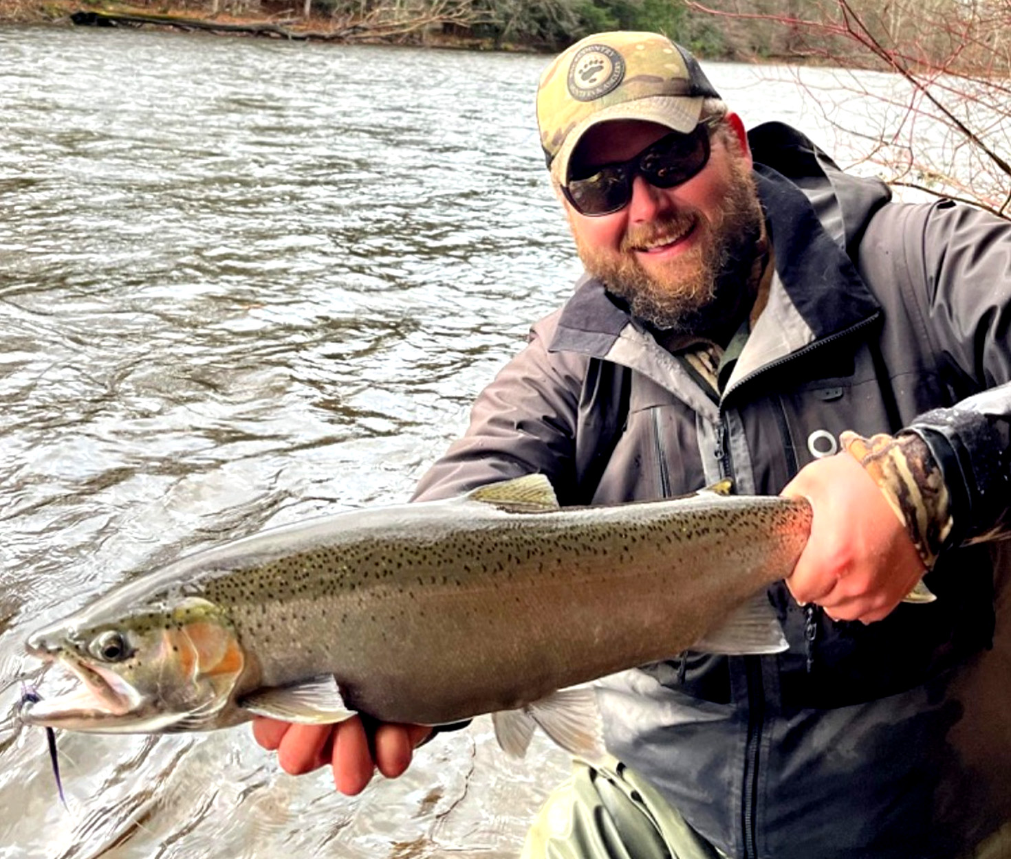 A fly fisherman holds up a steelhead caught in a Great Lakes tributary.