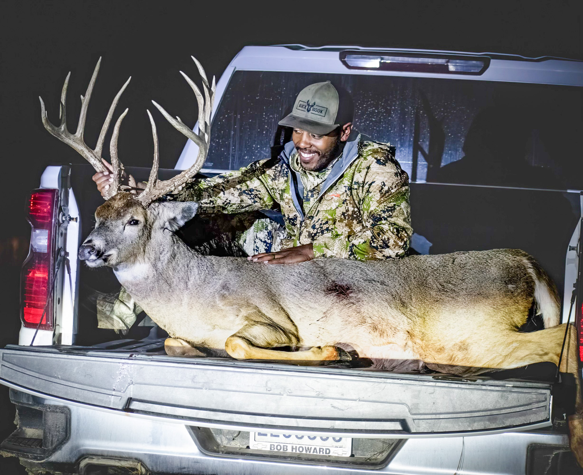 A bowhunter poses with a buck in the back of the truck.