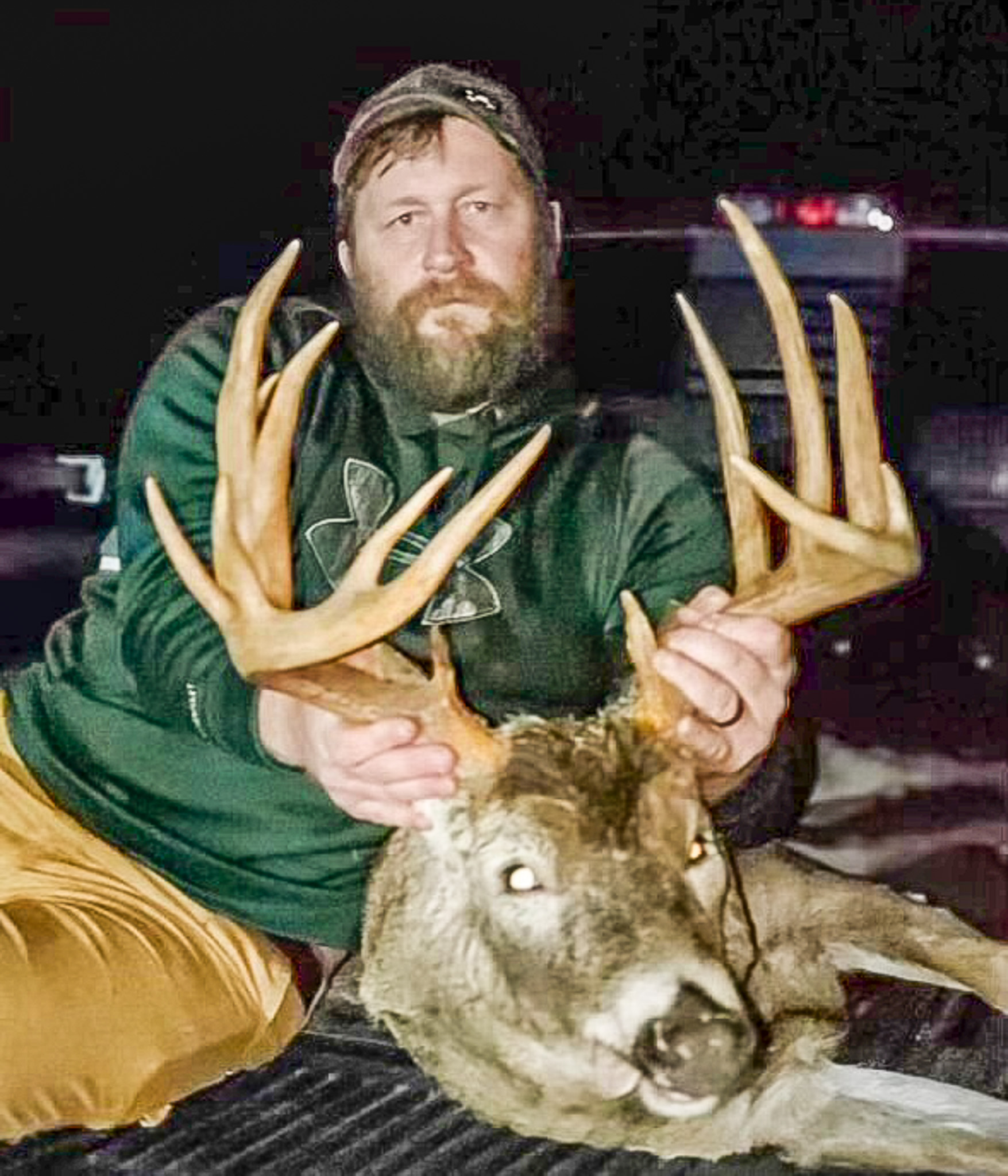 A man in a green hoodie holds up the antlers of a big public land buck.