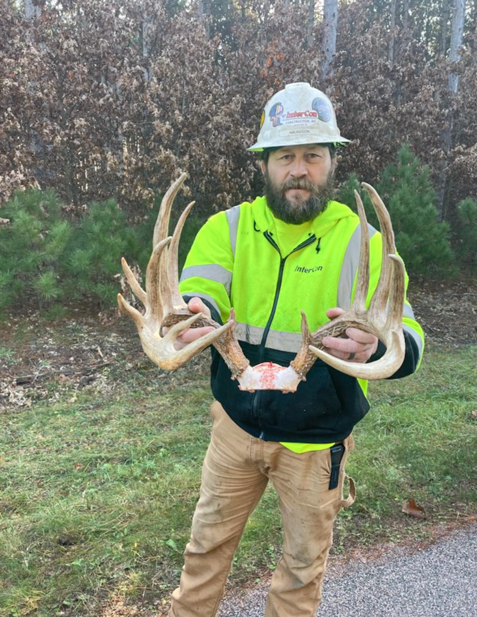 A man in a fluorescent shirt holds up antlers.