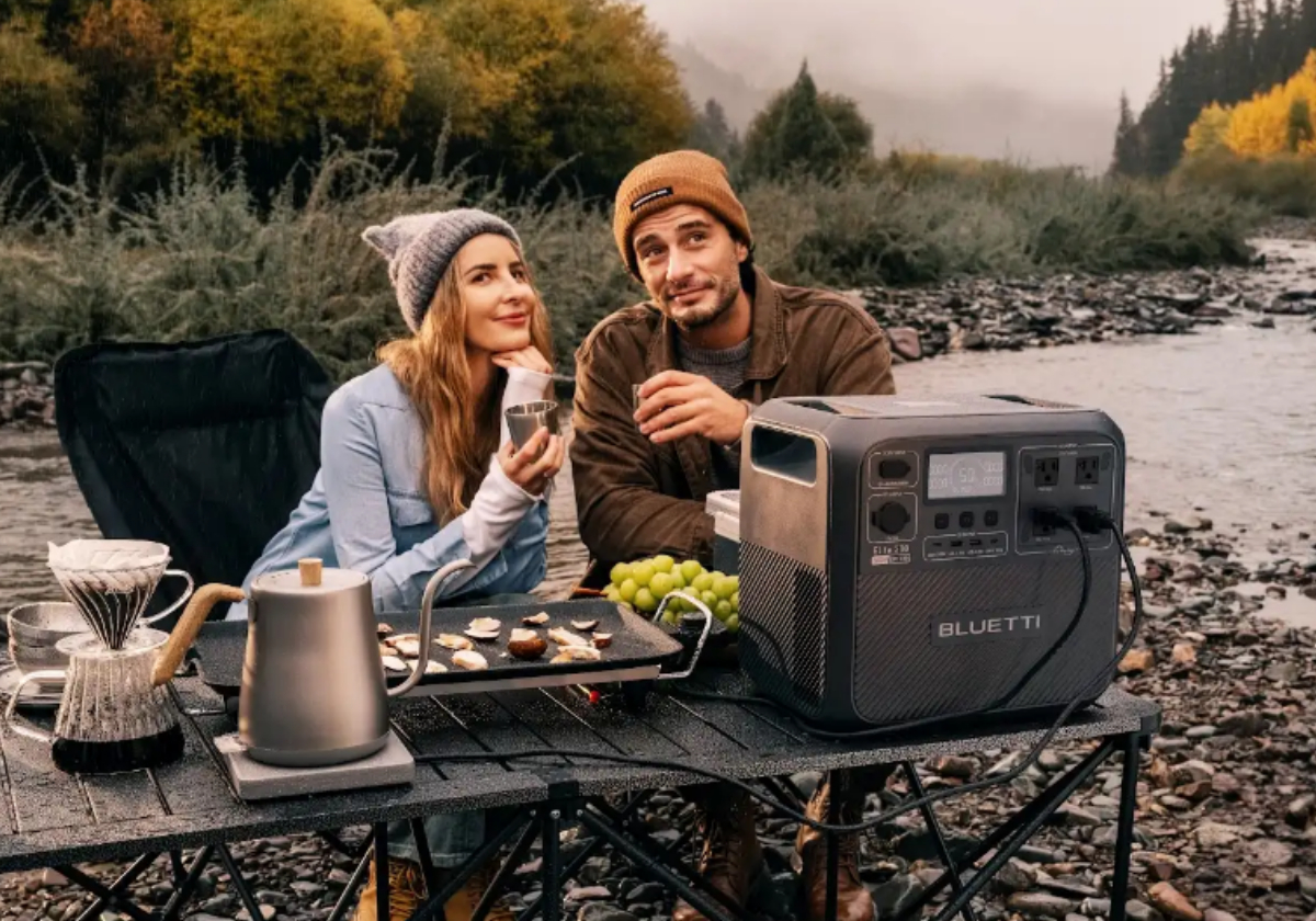 woman and man sitting at camping table with appliances plugges into a Bluetti and enjoying coffee and the scenery