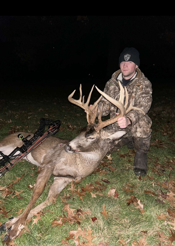 A bowhunter with a nice buck in a pasture.