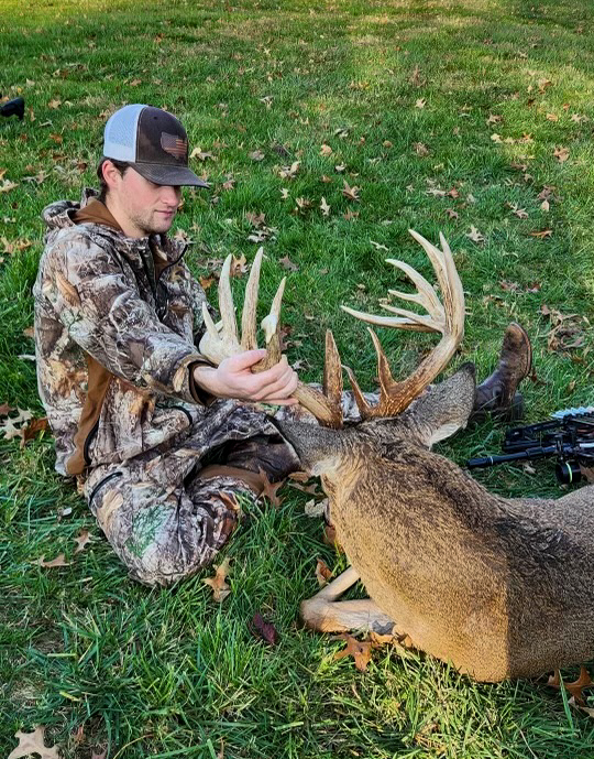 A hunter looks at a big buck while in the grass.