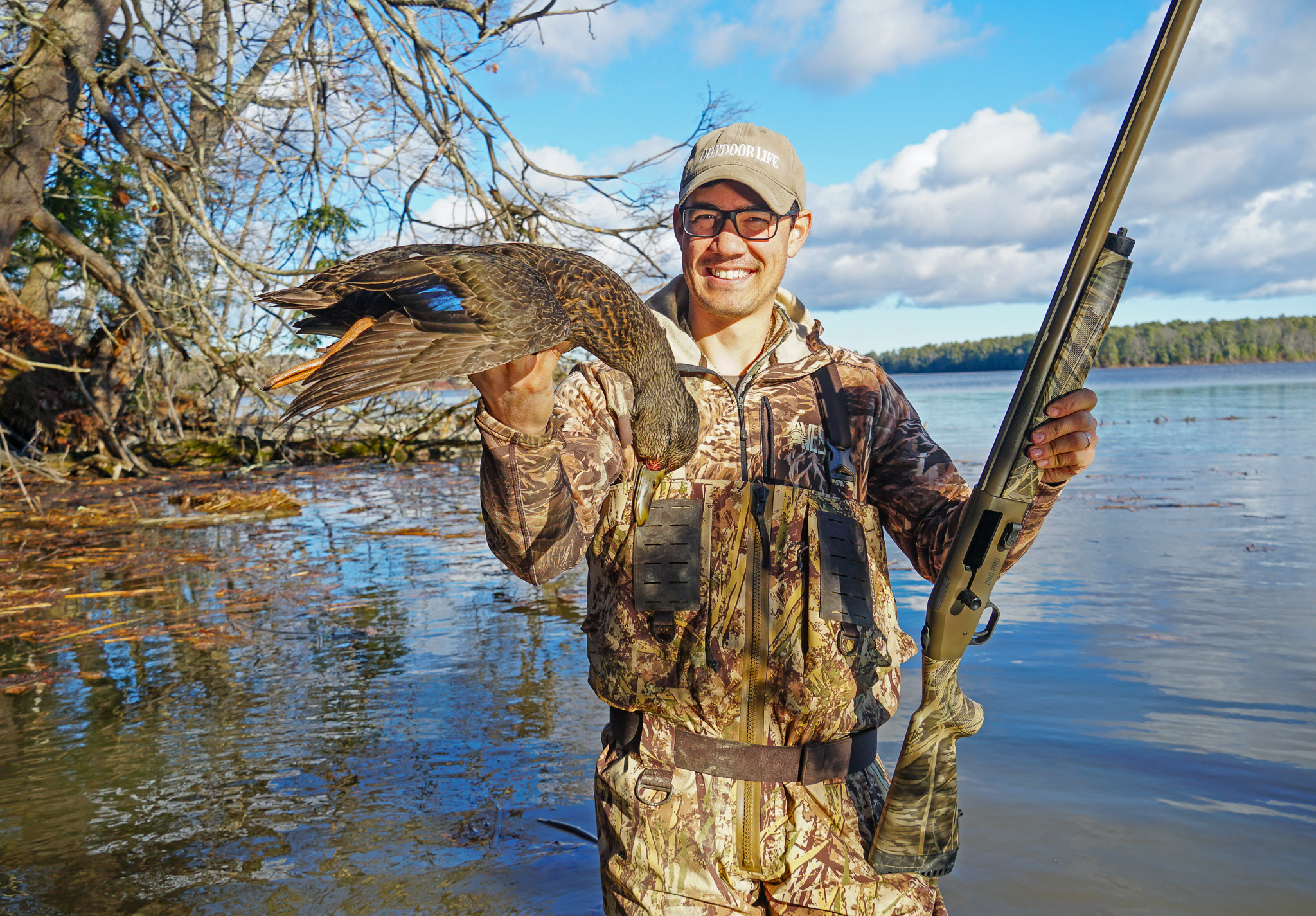 A hunter holds up a nice black duck and a shotgun.