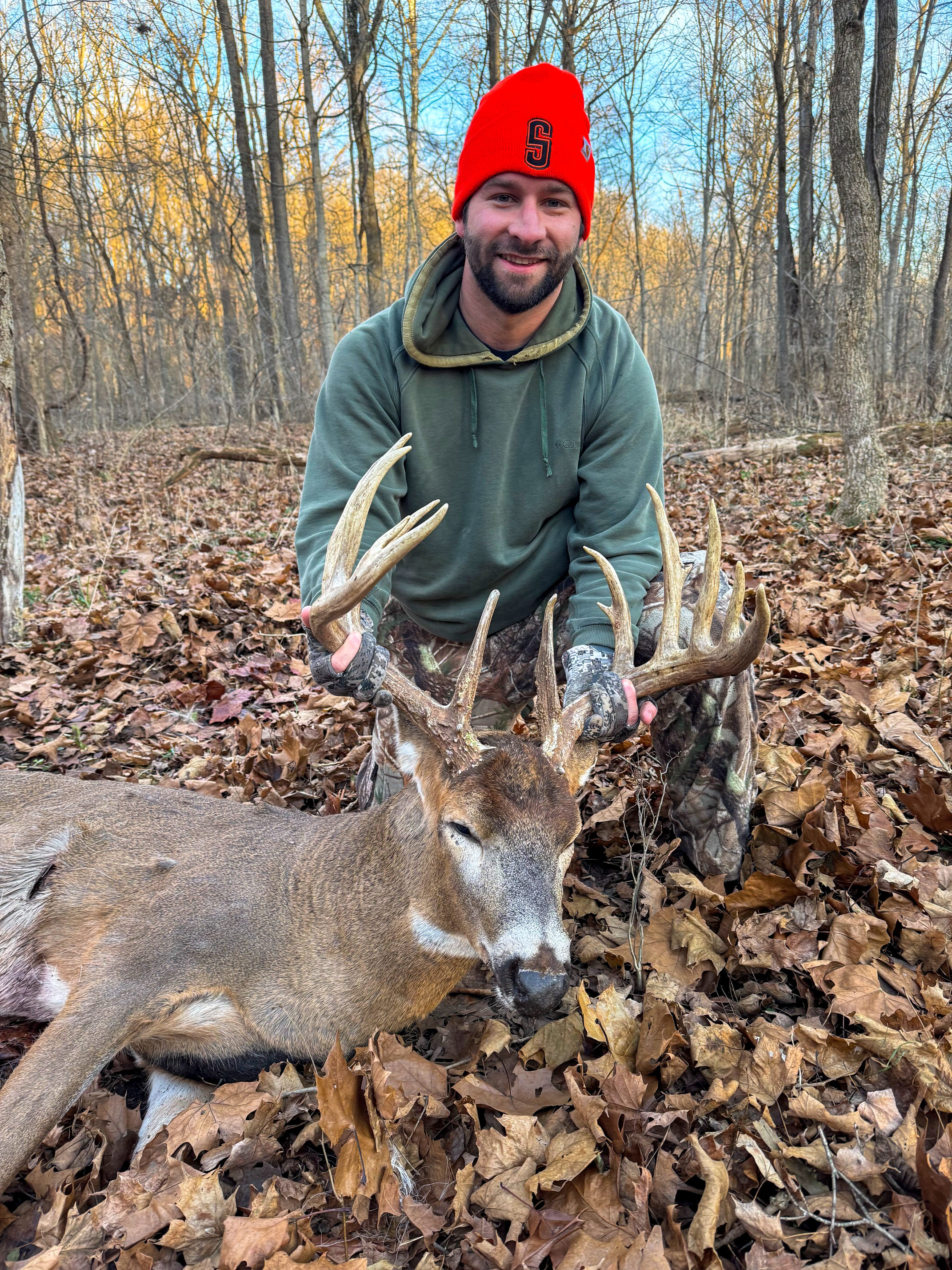 A hunter kneels beside a nice buck in the leaves.