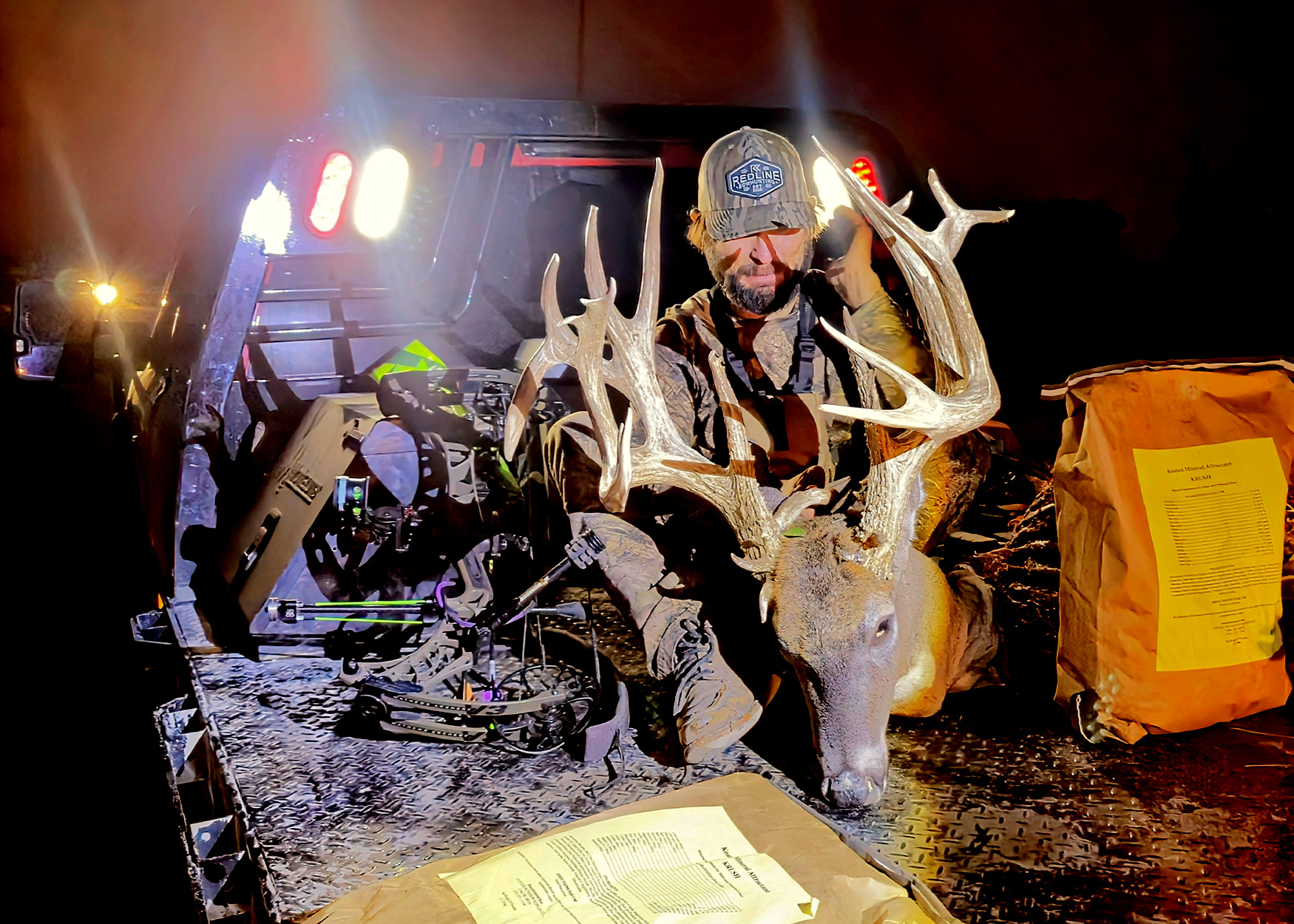 A bowhunter admires a buck in the bed of a truck.