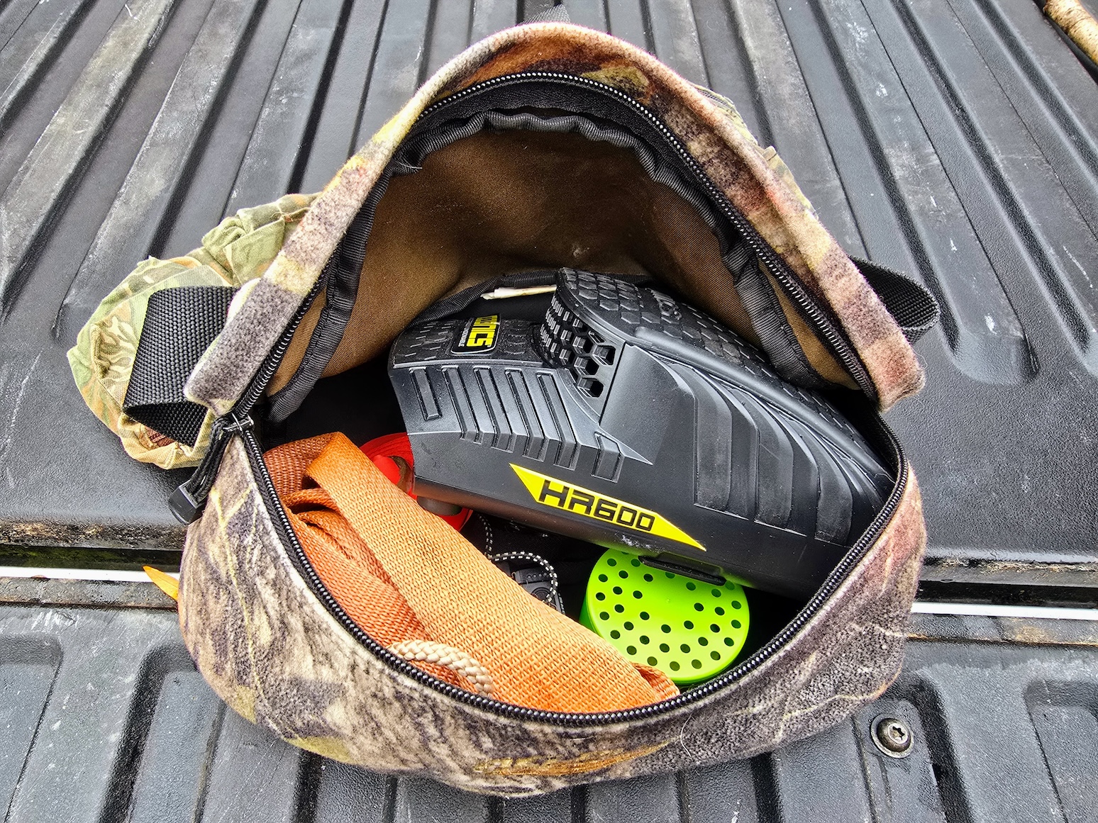 A camo fanny pack on a truck tailgate is zipped open to reveal an Ozonics HR600 amongst other gear.