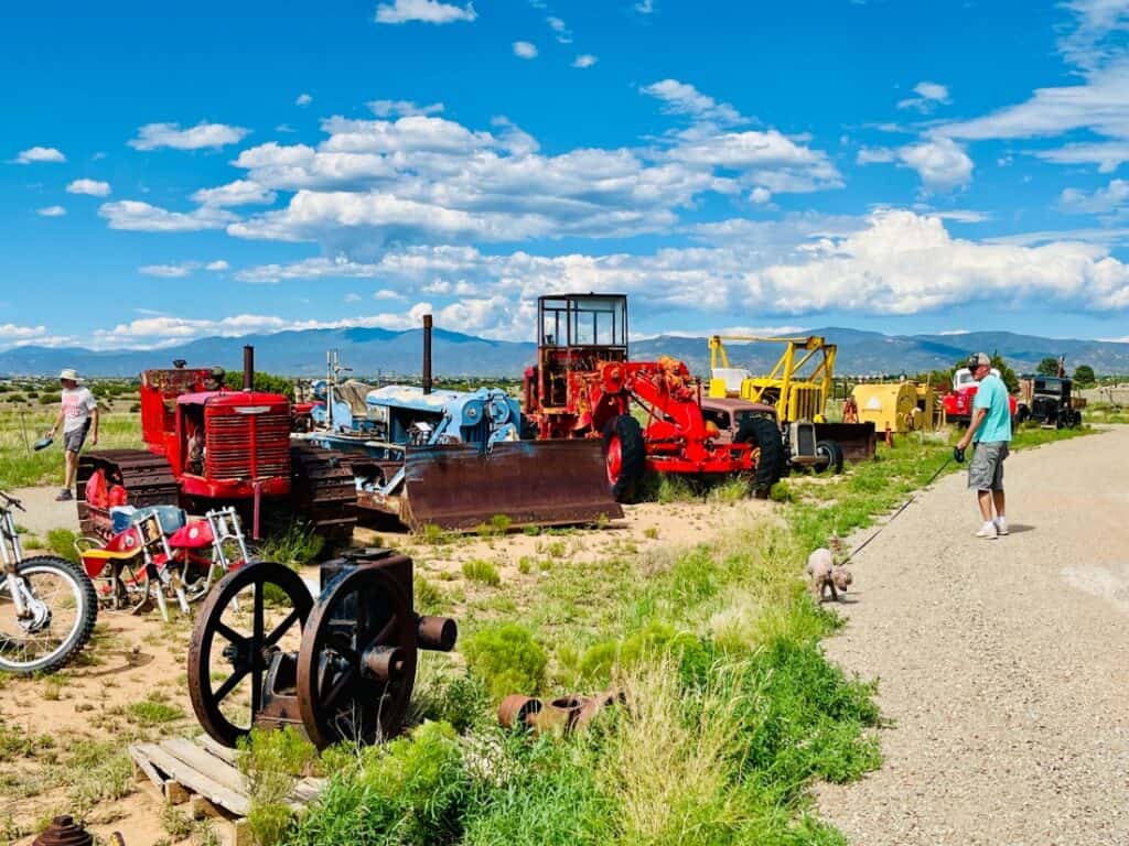 A man walks his dog near Santa Fe Skies RV Park. He is viewing agricultural equipment on the side of the road.