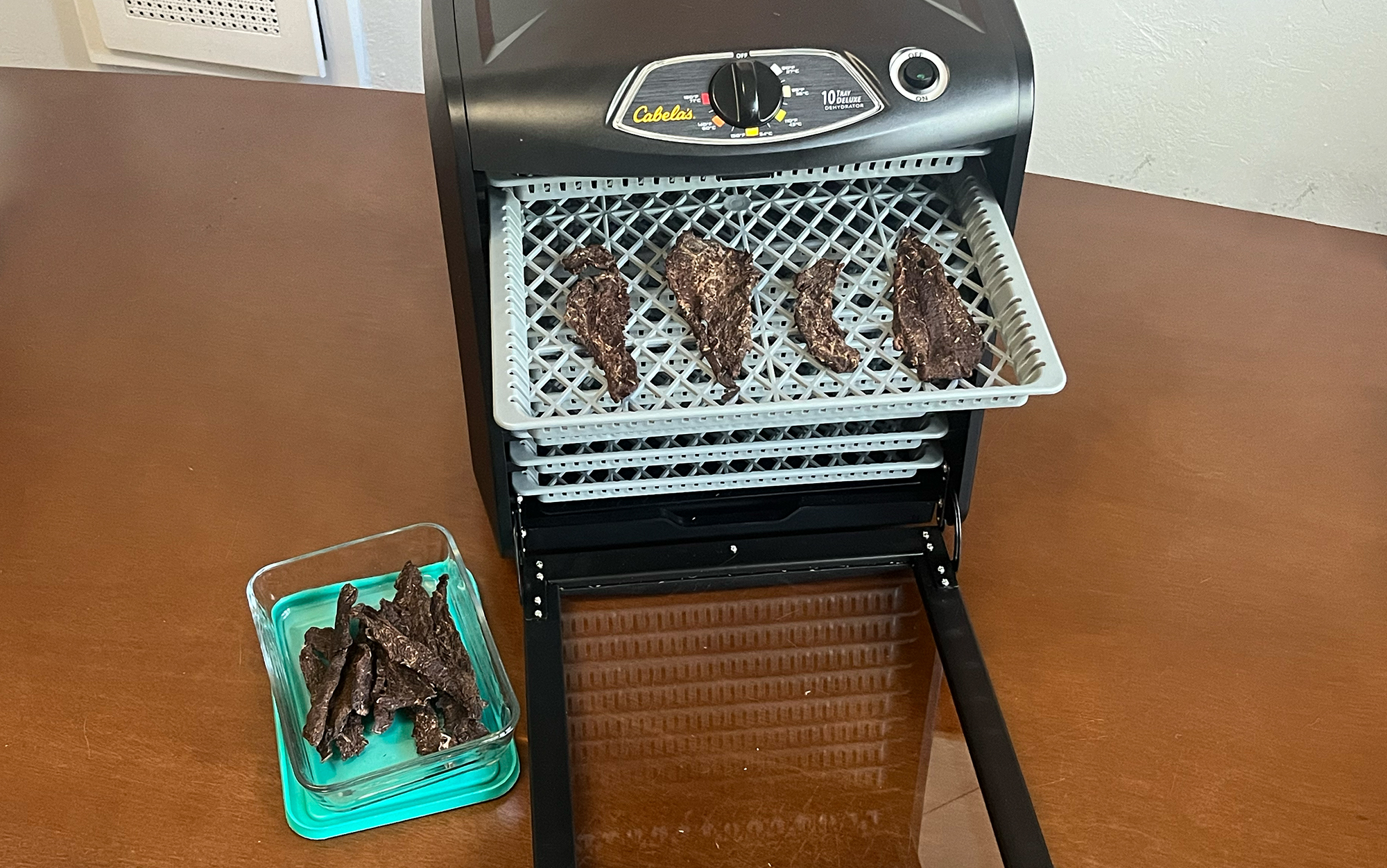 The Cabela's dehydrator sits on a table with jerky inside.