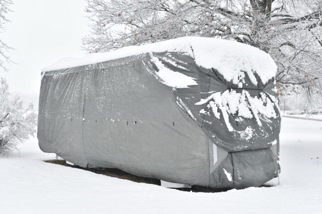 A Class A motorhome under an RV cover in snowy weather.