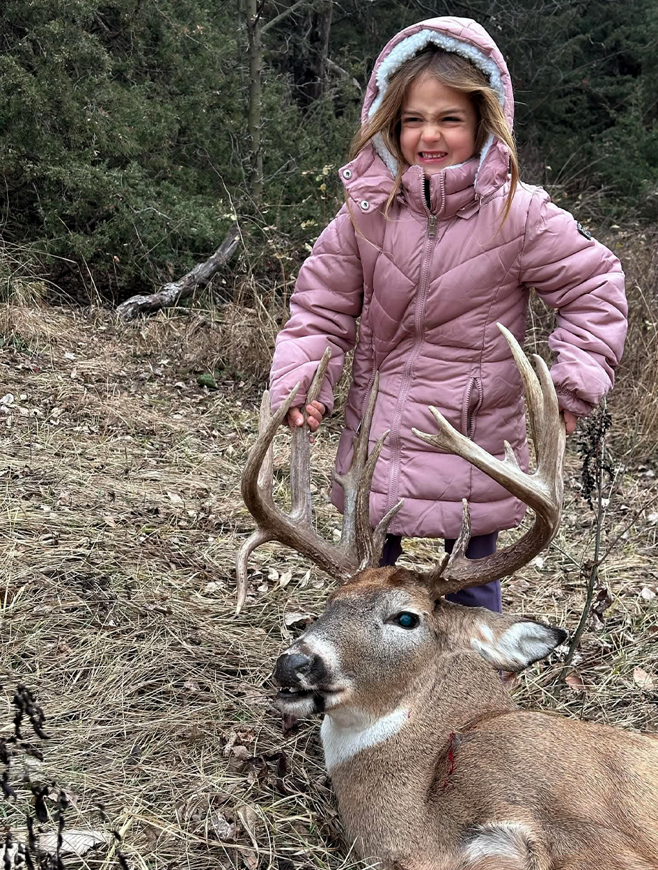 A hunter's daughter holds up his whitetail buck.