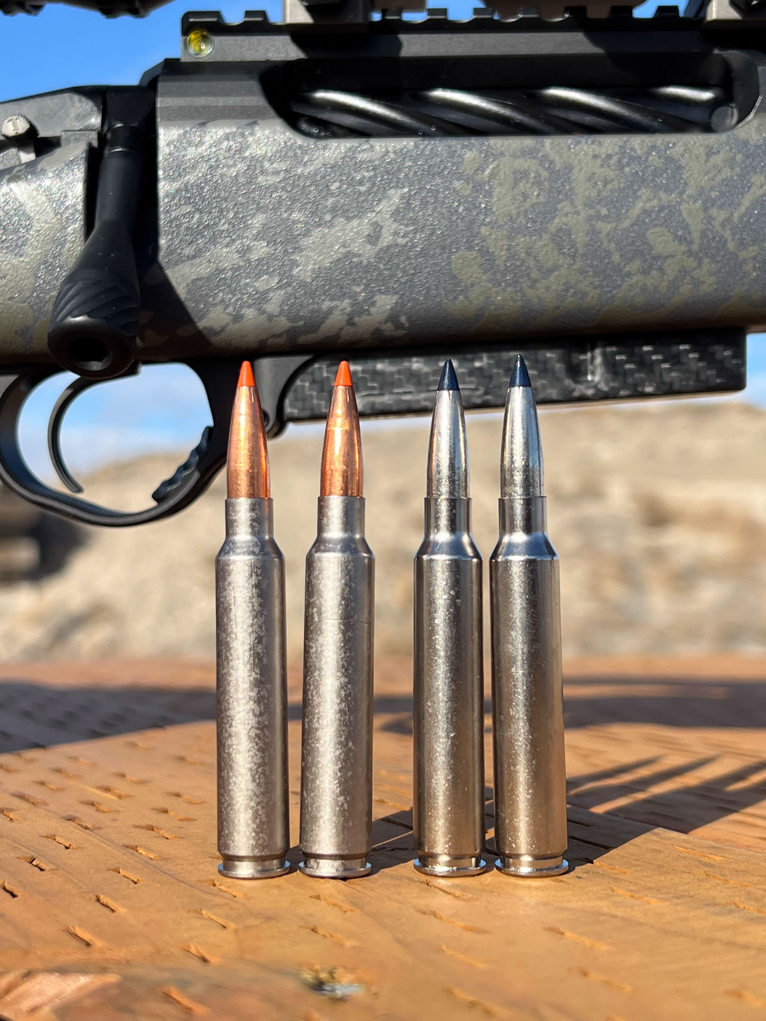 Four rounds of 7mm Backcountry ammunition in front of a rifle