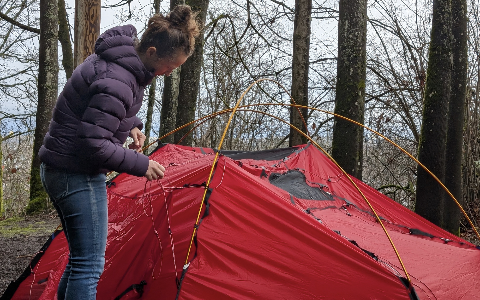 A woman in a purple jacket clipping the tent body to the poles of the HIlleberg Allak 3