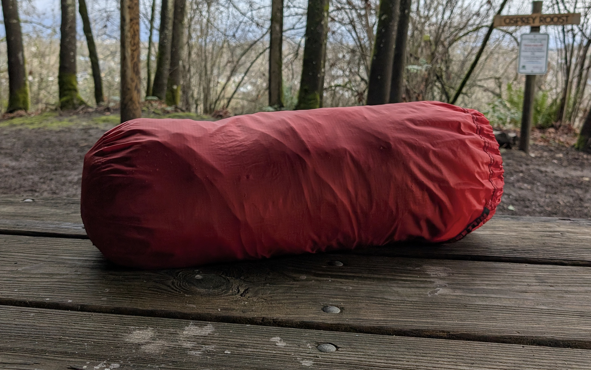 A packed Hilleberg Allak 3 sitting on a picnic table on a forested ridge.