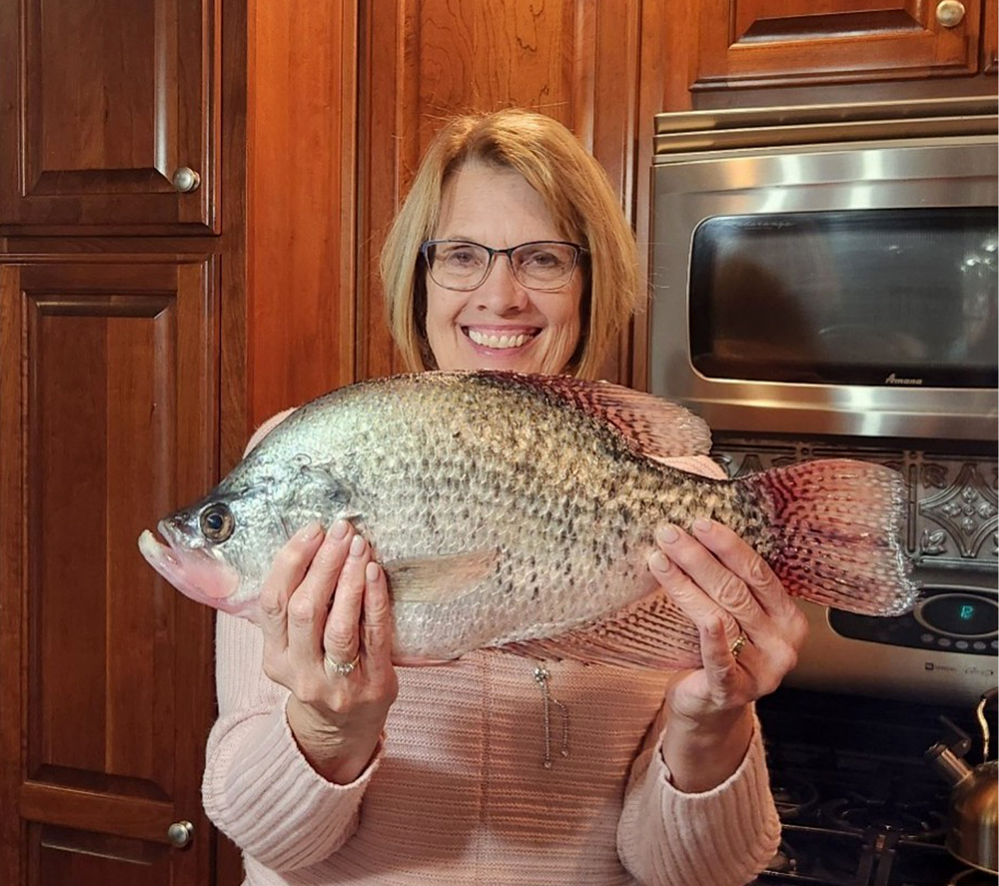 An angler holds up a crappie in her kitchen.