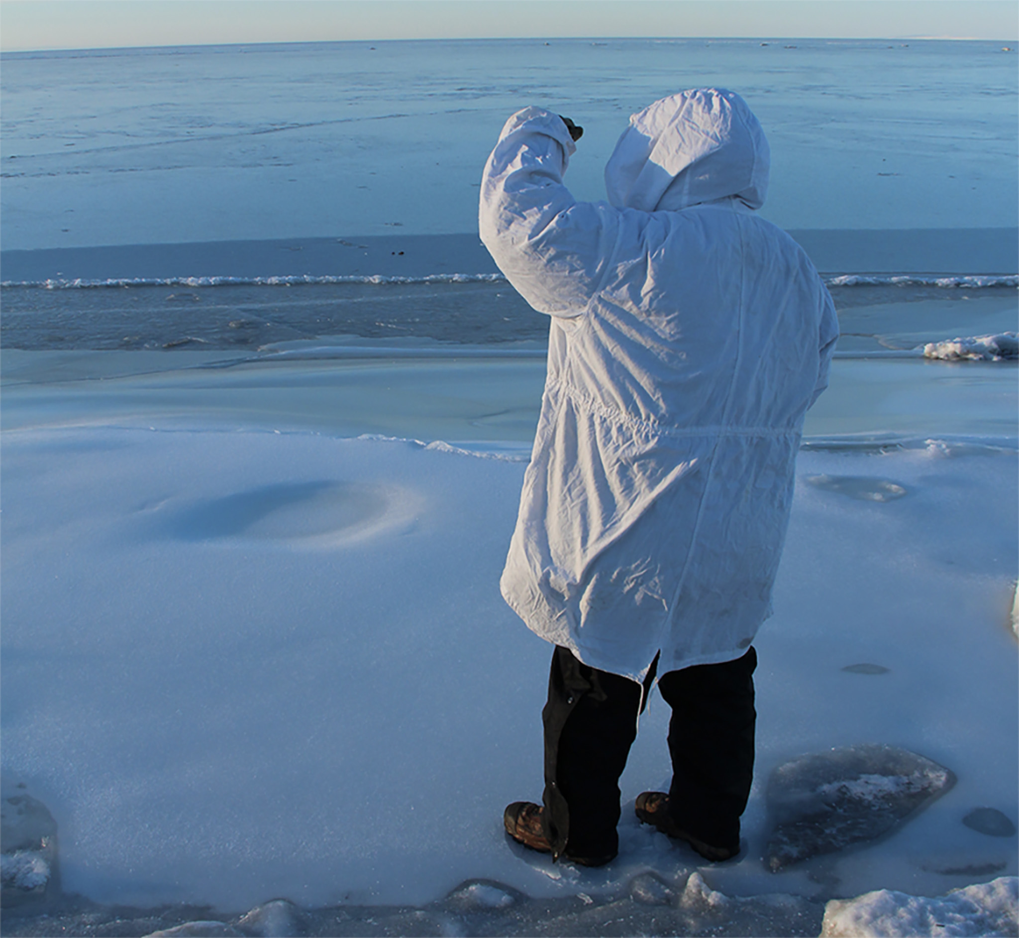 A man looks out over the edge of the Arctic Ocean.