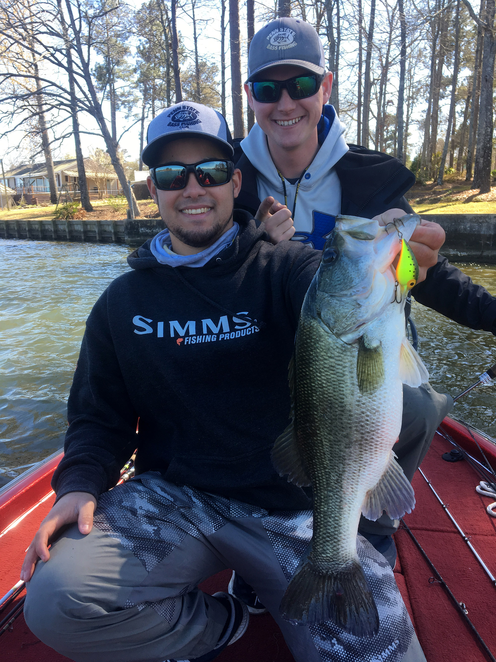 A guy holds up a bass in caught while fishing in the winter.