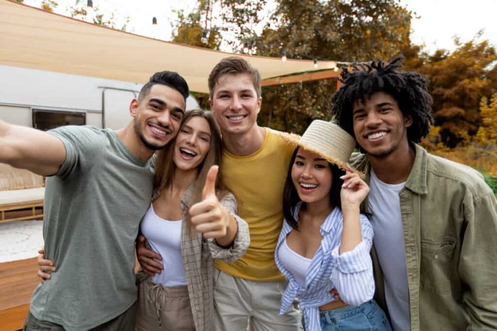 Group of cheery diverse millennials taking selfie together near an RV.