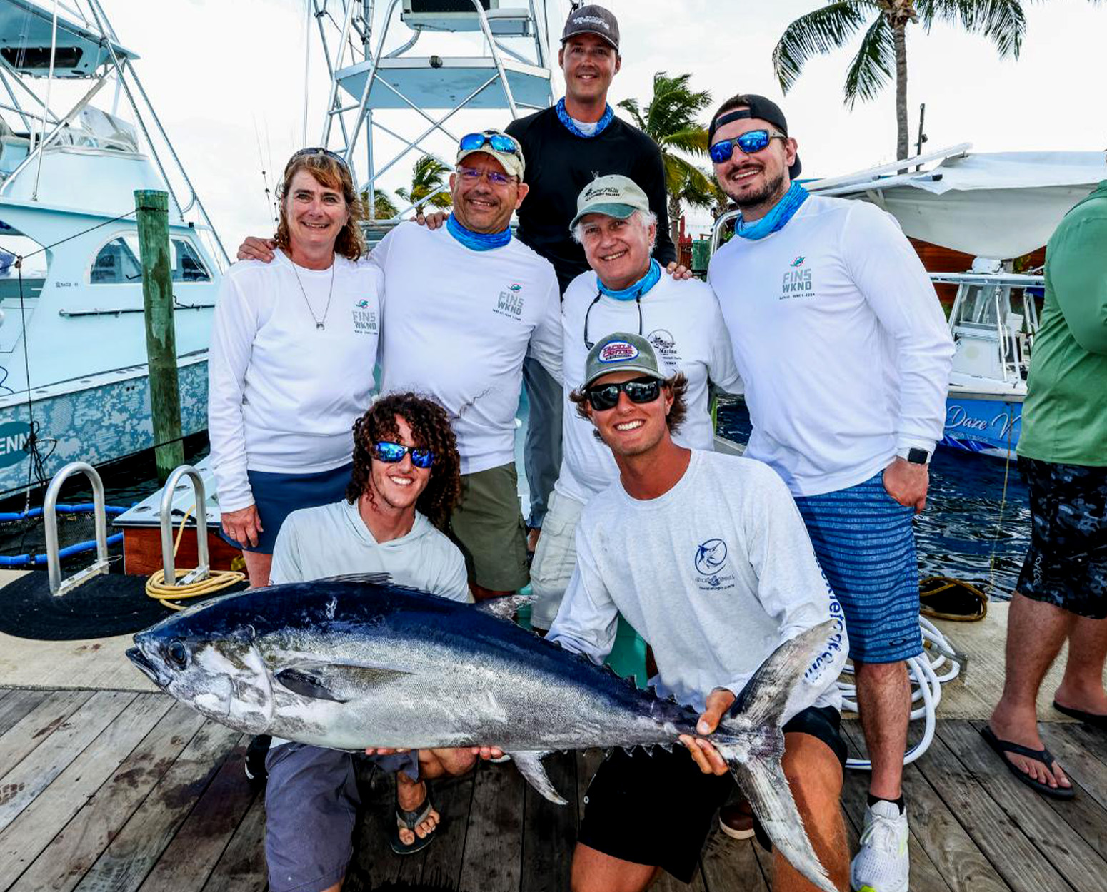 Six people pose on a dock with a large blackfin tuna. 