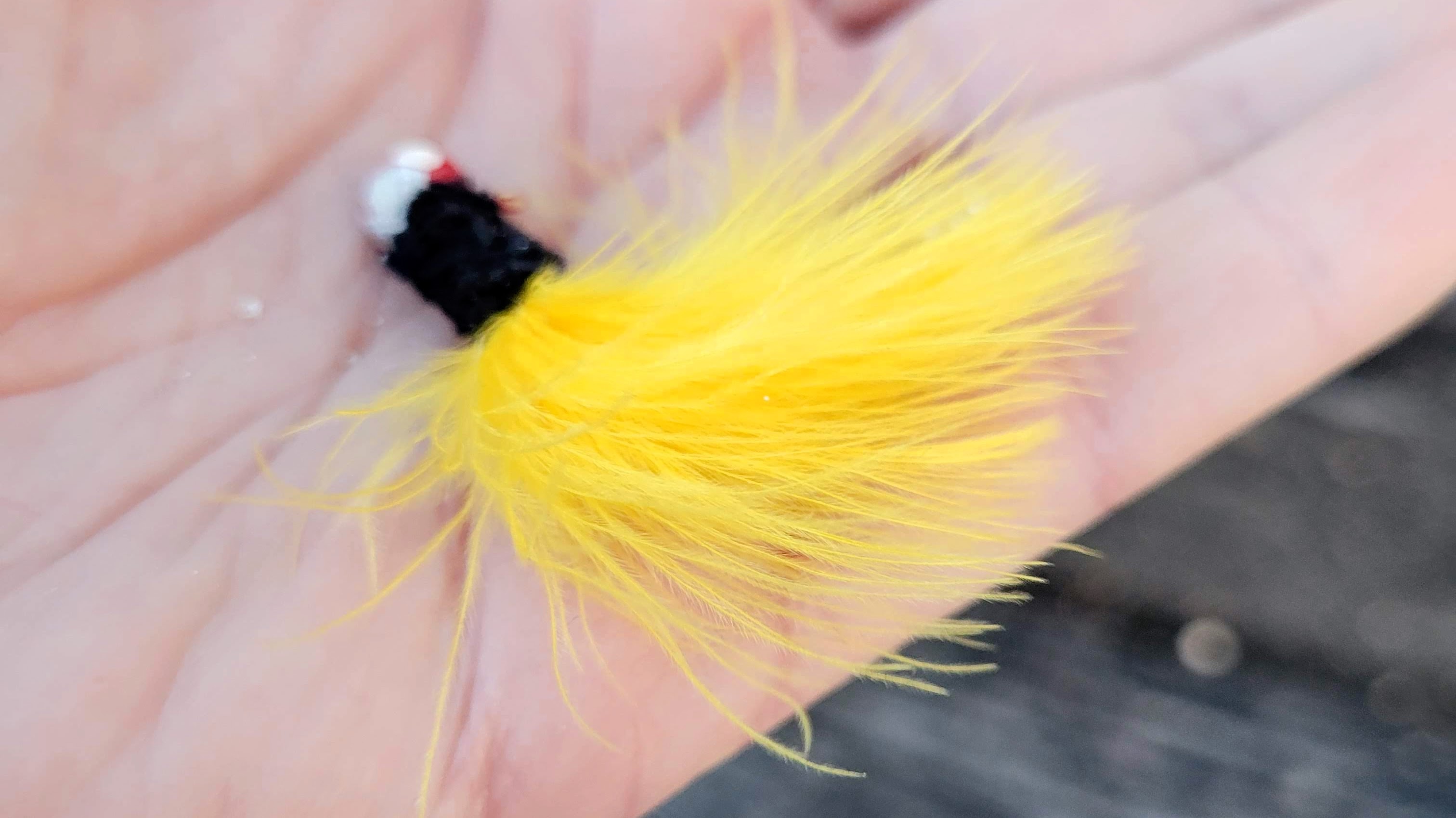 A fluufy yellow and black marabou jig lays in the palm of a hand.