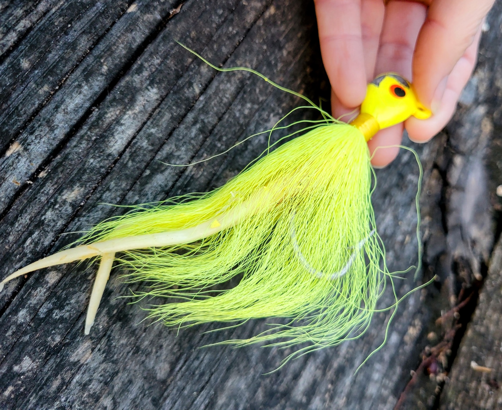 A hand holds a chartreuse bucktail with a yellow head and a soft plastic trailer.