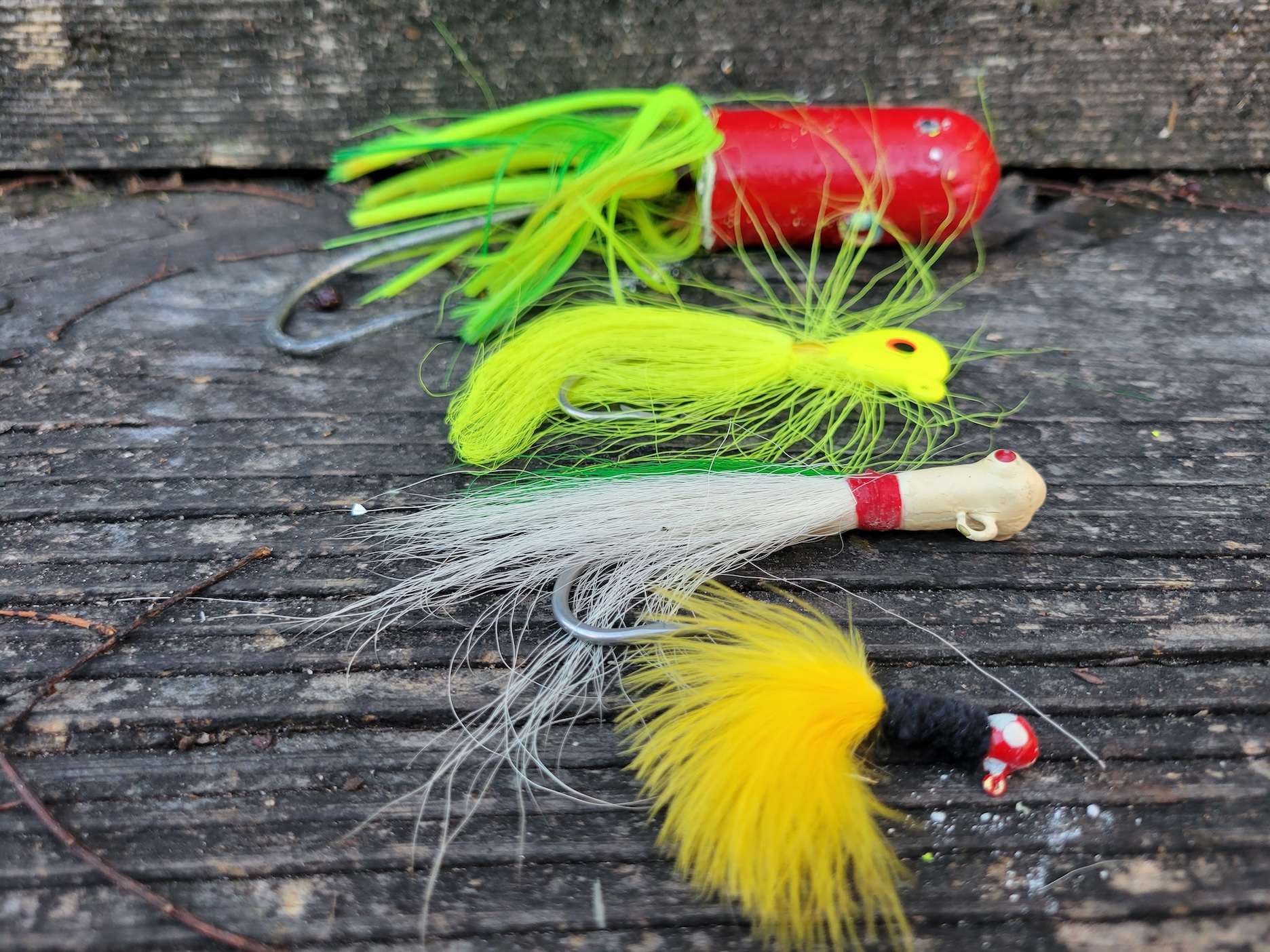 Three different bucktail designs lay in a row, including a small yellow marabou jig, a classic white bucktail jig, a chartreuse hair jig with a flat head, and a large lead head tuna jig.