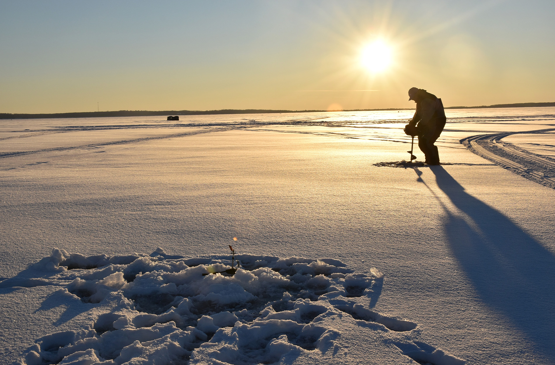 Ice fisherman drills holes on the frozen surface of a lake.