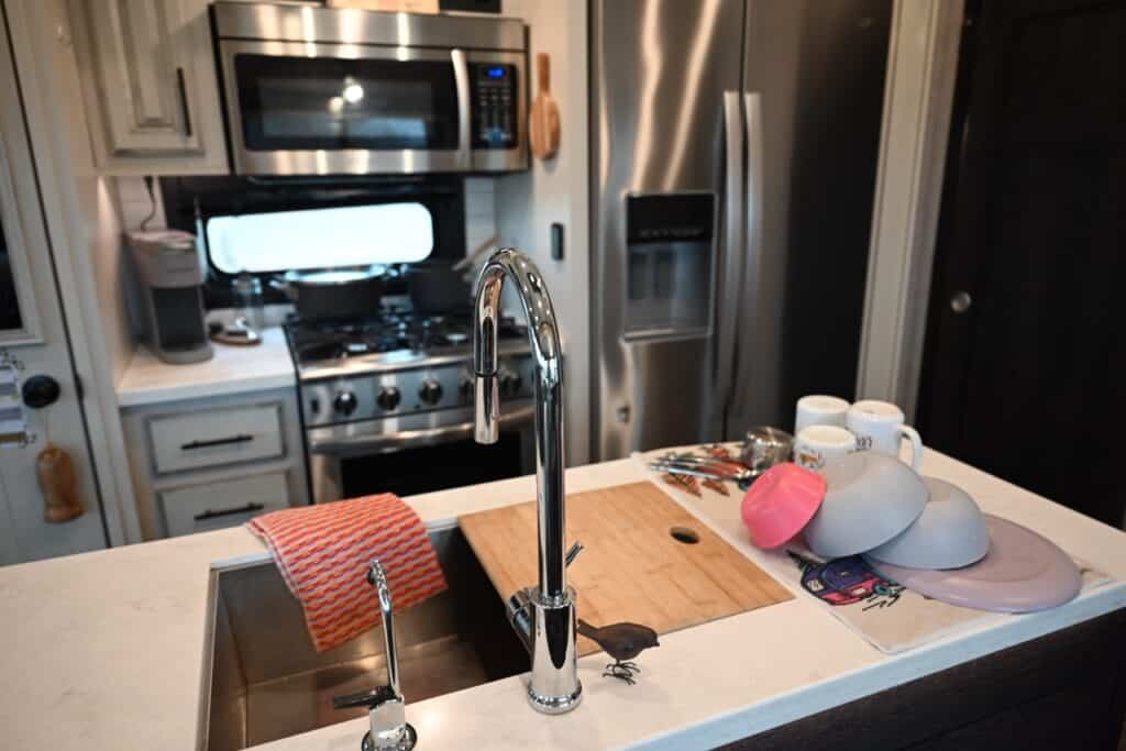 An RV galley, including island sink, convention microwave, stove, and single-cup coffee maker.