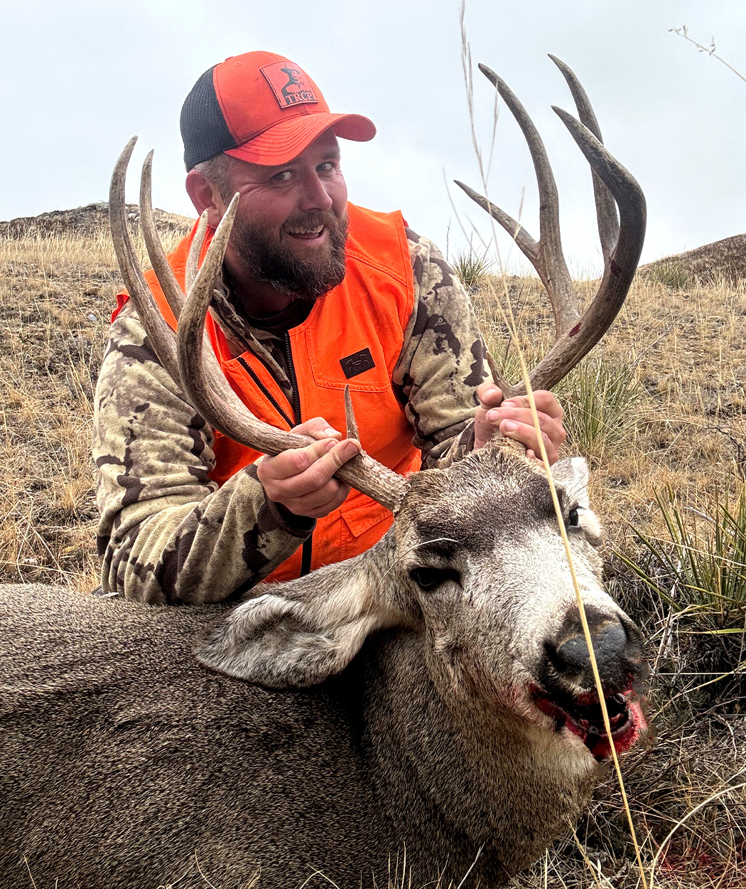 A hunter holds up a mule deer buck for the camera.