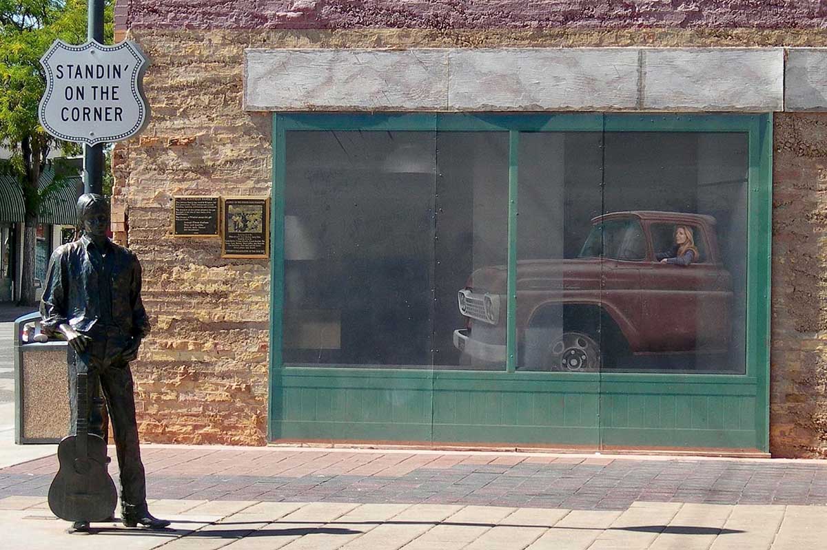 A statue of young man with a guitar and a truck reflected in a window.