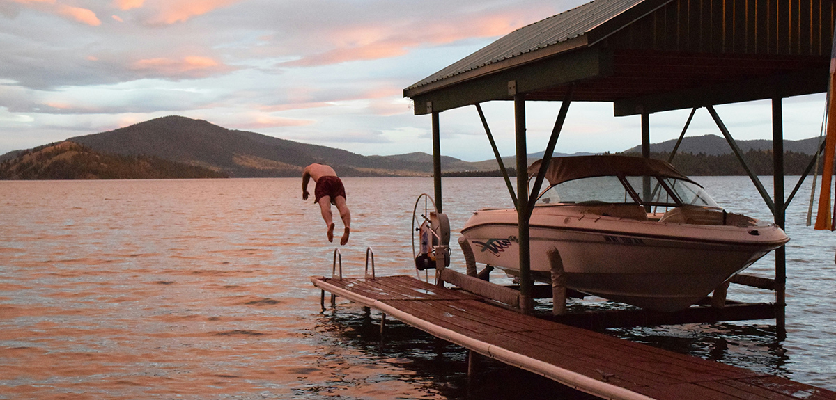 Man diving off dock into lake near dry-docked boat.