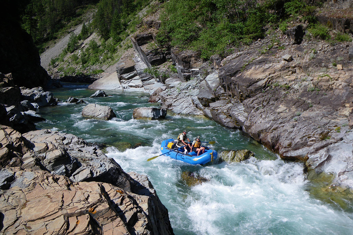 Two passengers in a blue raft that careens down a violent stretch of whitewater river. 