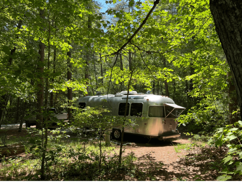 An airstream trailer is tucked away in a beautiful and protected campsite.