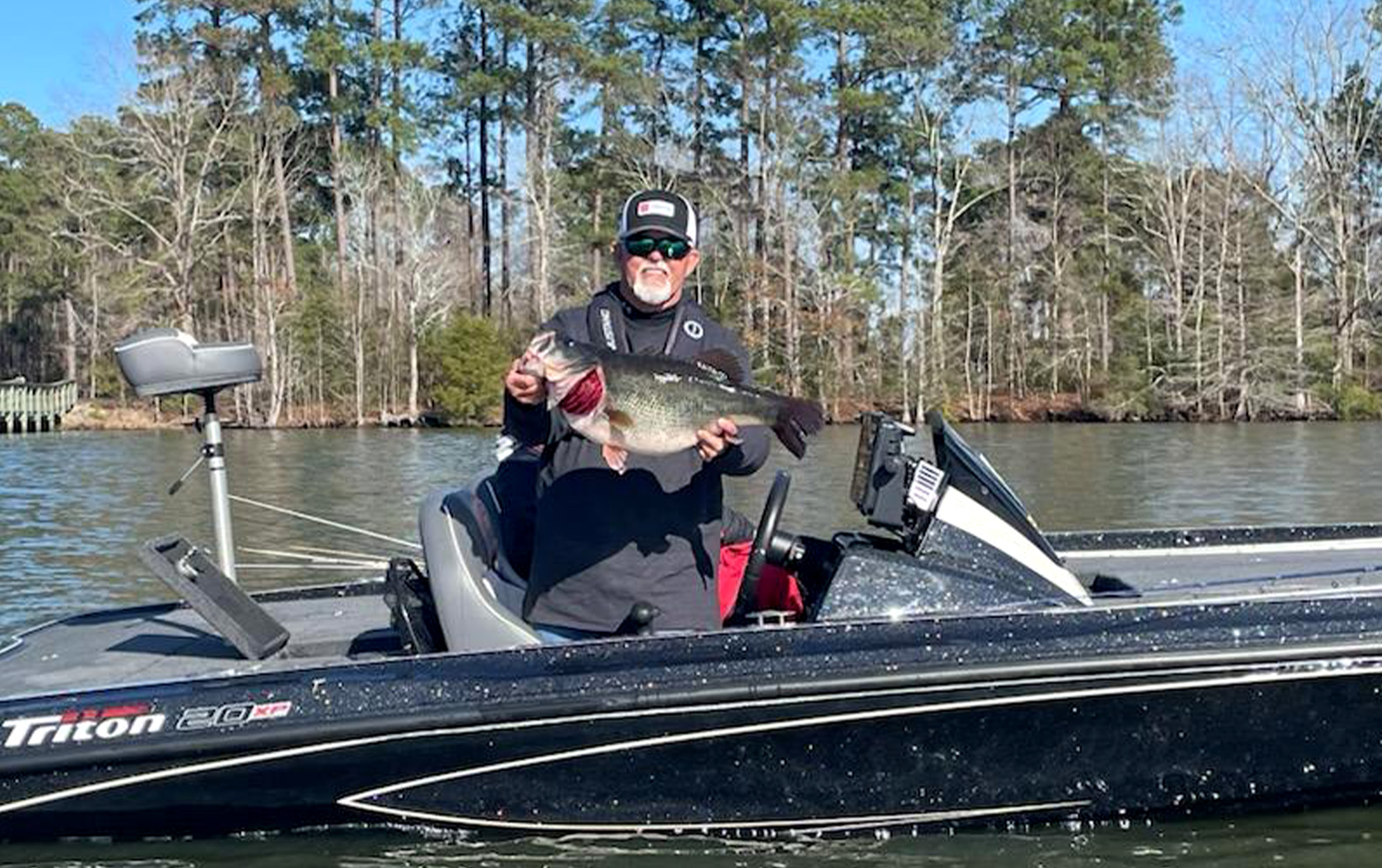 An angler in a bass boat holds up a largemouth bass.