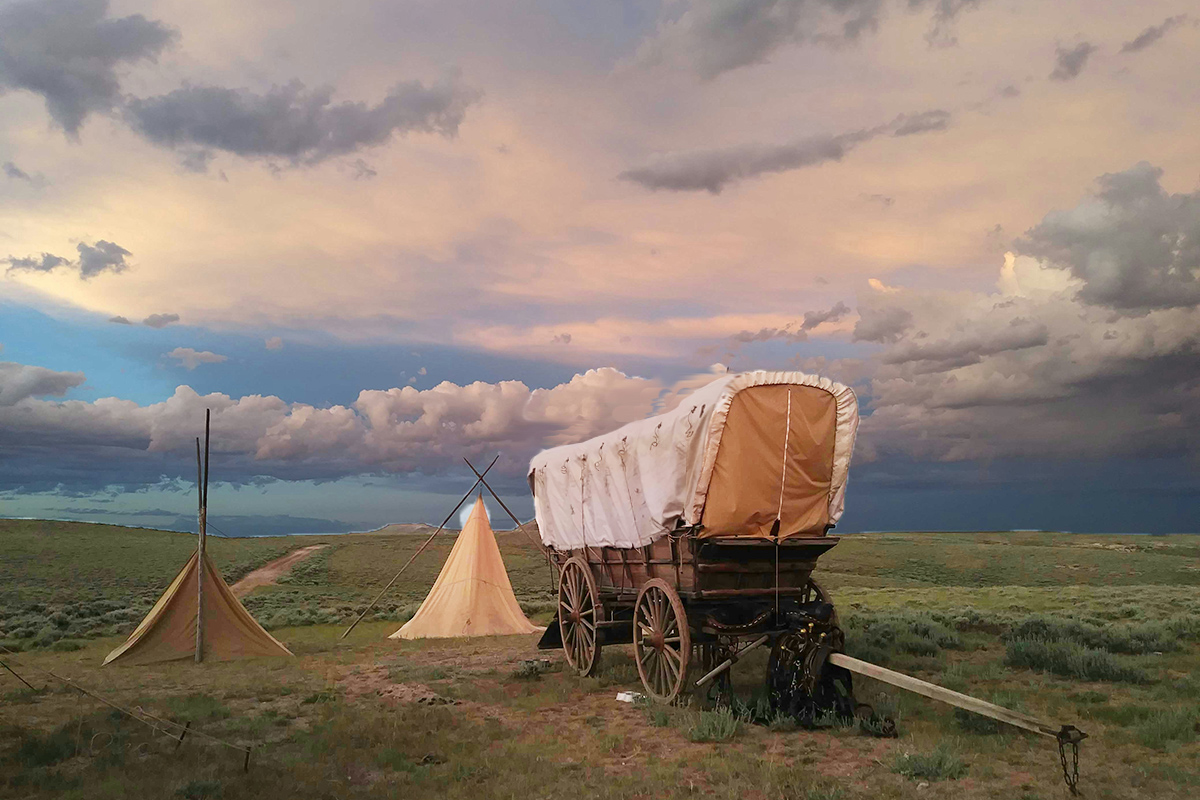 Pioneer wagon on grassy ground against a cloudy sunset sky.