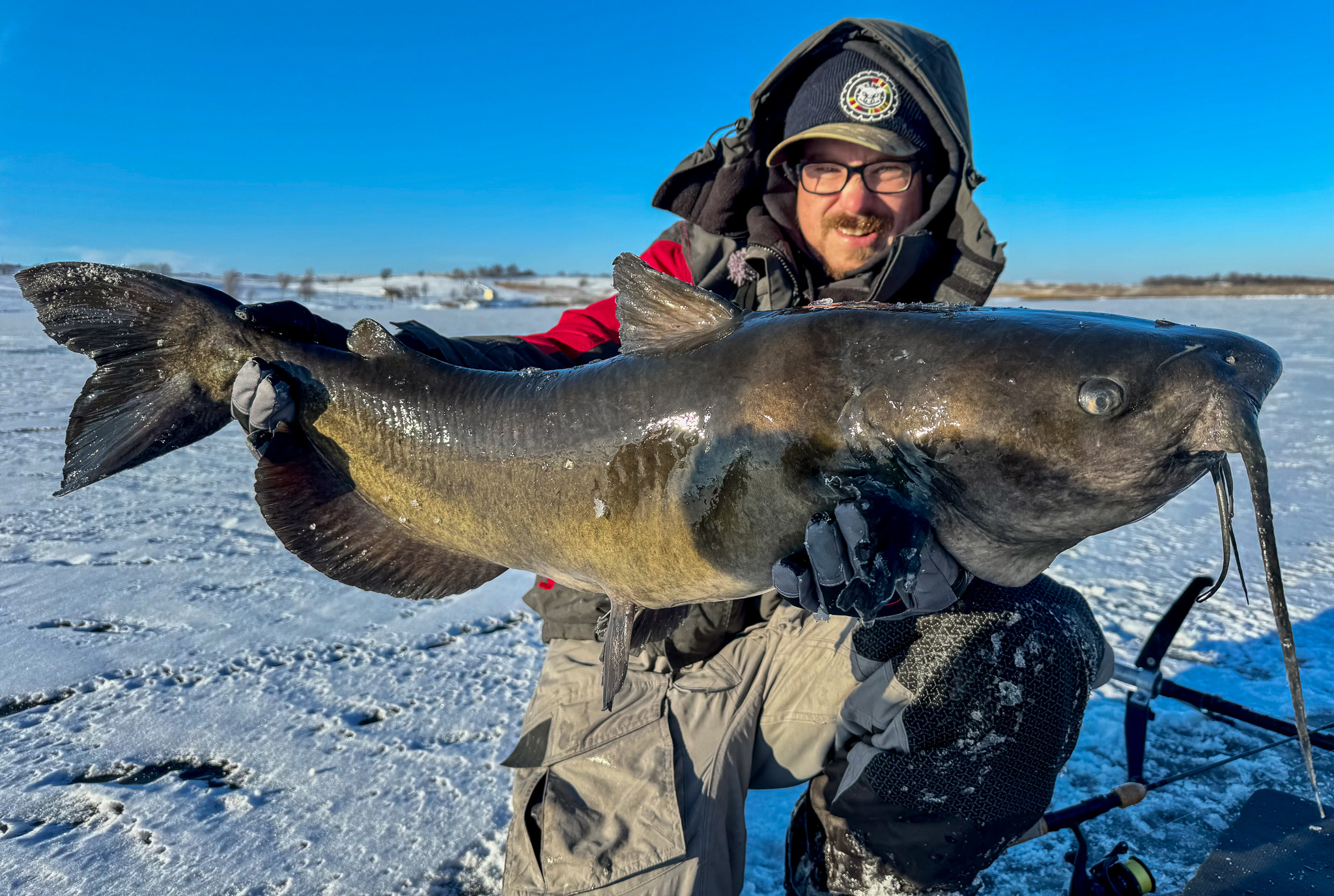 An ice fisherman with a catfish kneels on the cie.