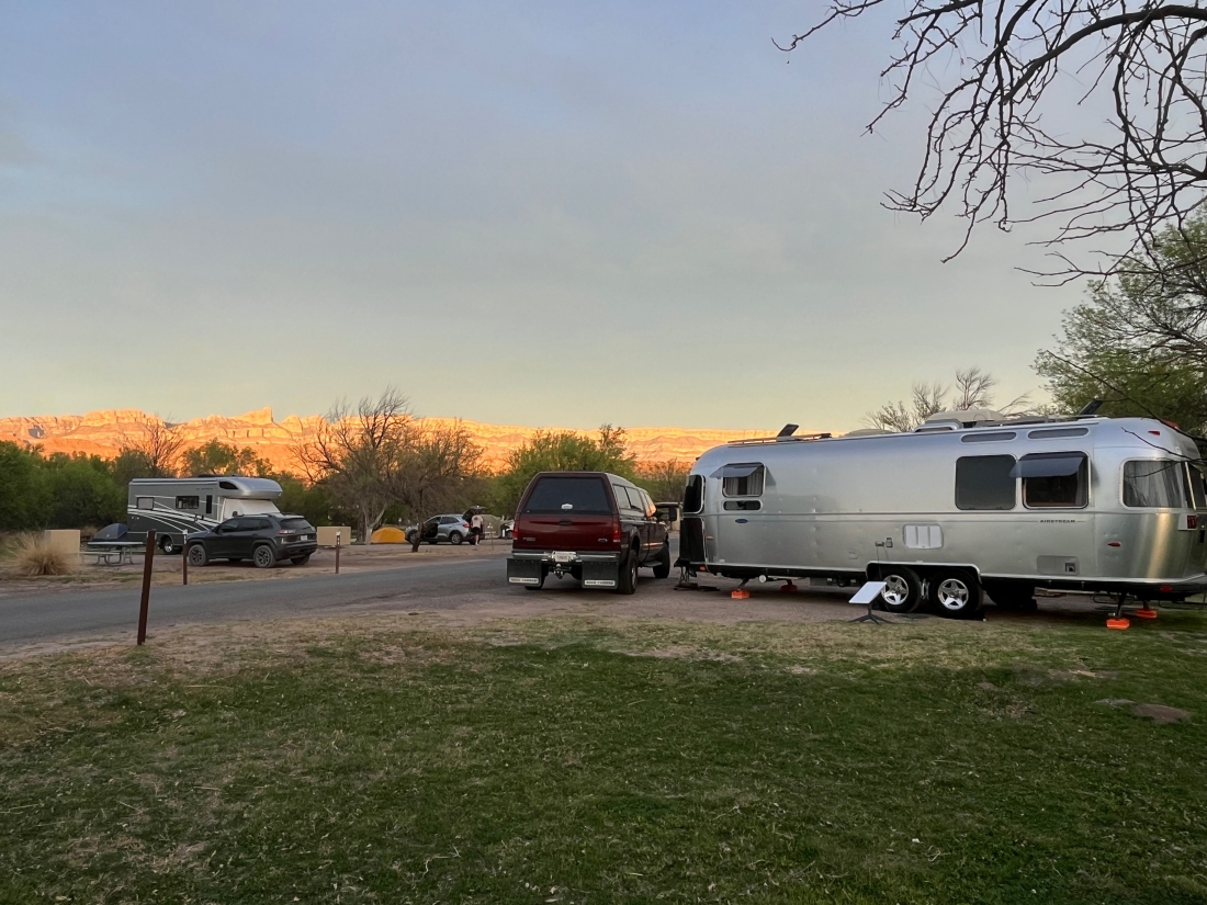 A trailer and trucks in a campsite.