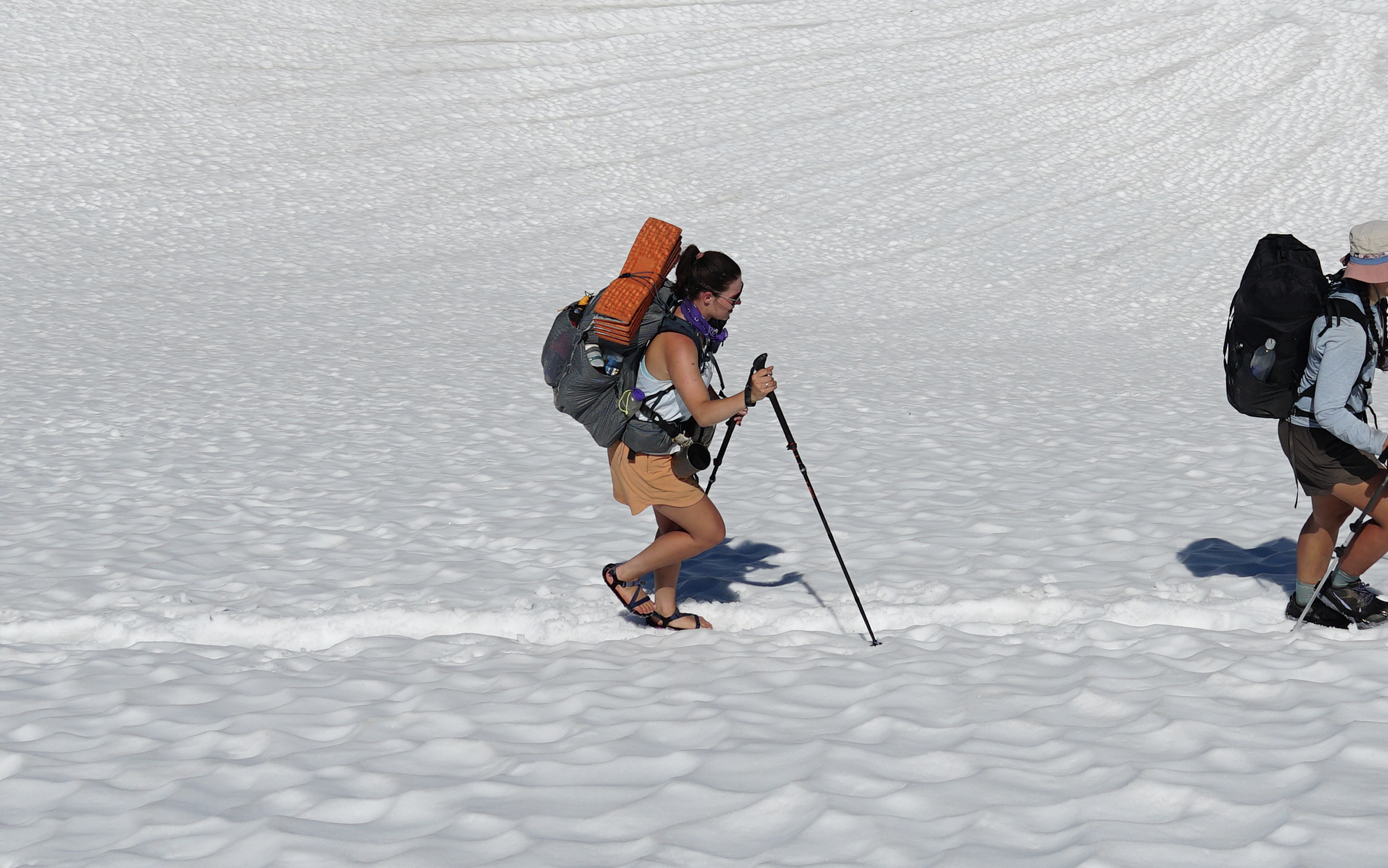 Woman backpacking across a snowfield wearing sandals