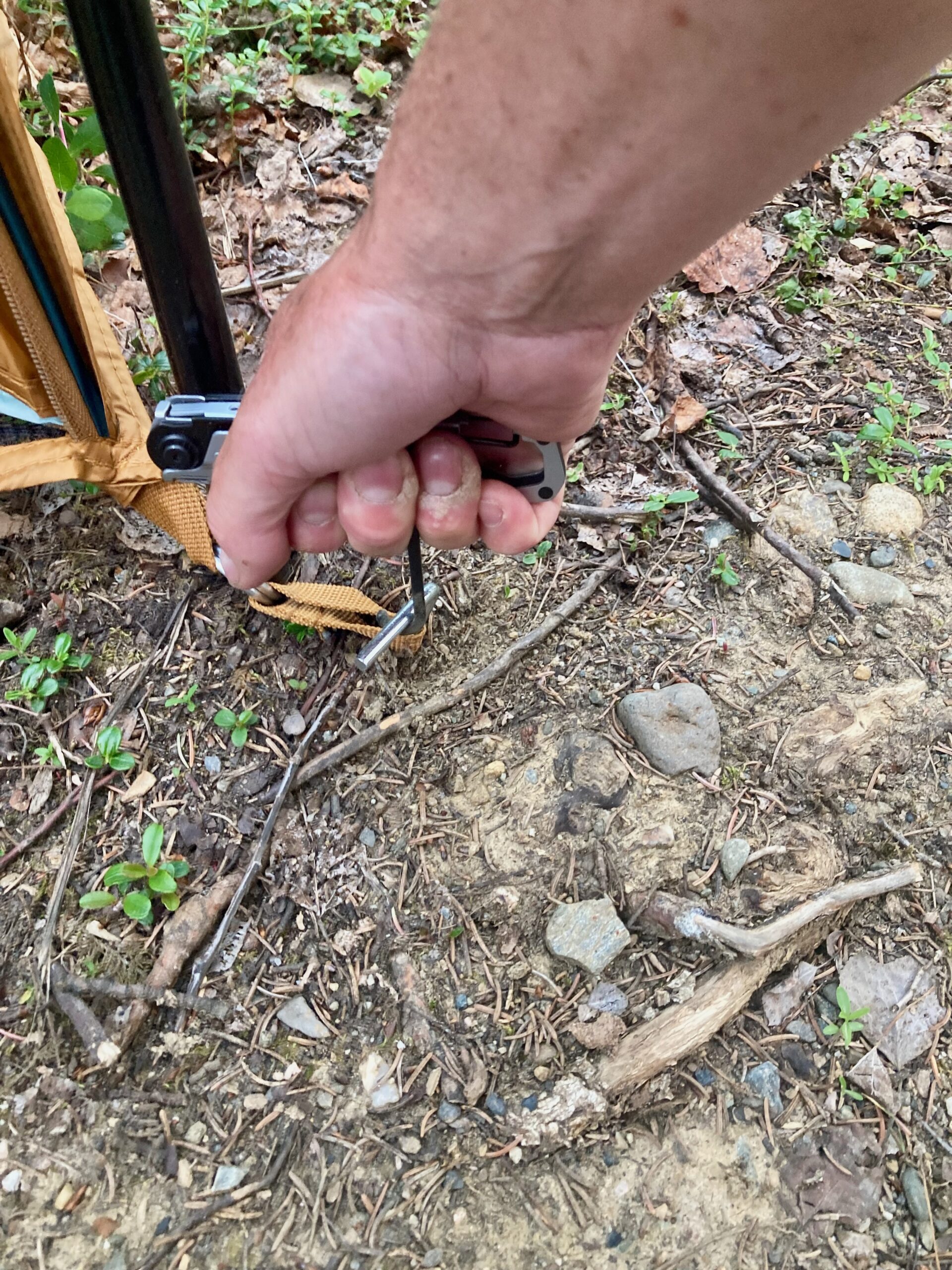 A hand uses a camping gadget to drive a tent stake. 