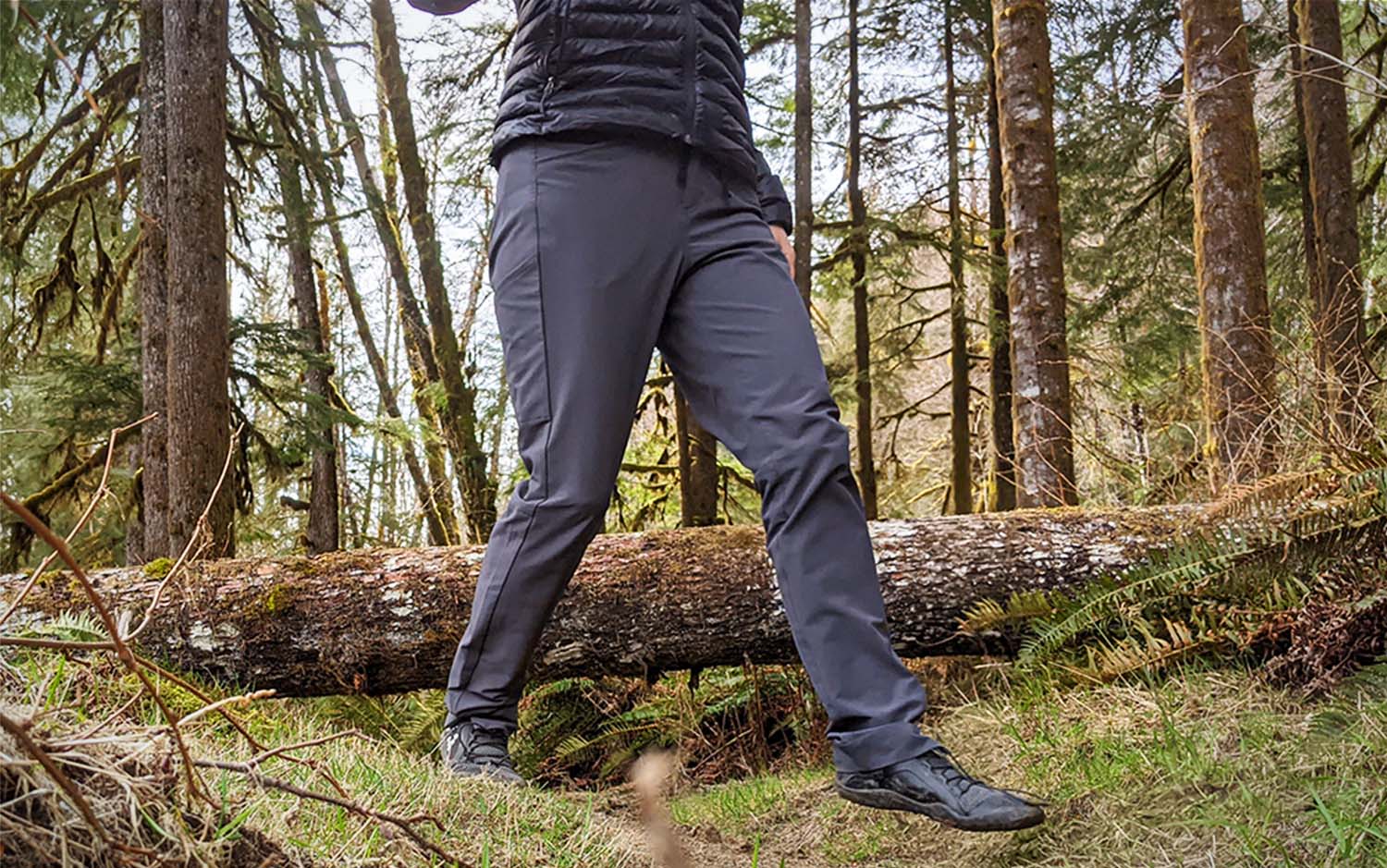 A person from the waist down walking in the woods wearing grey pants